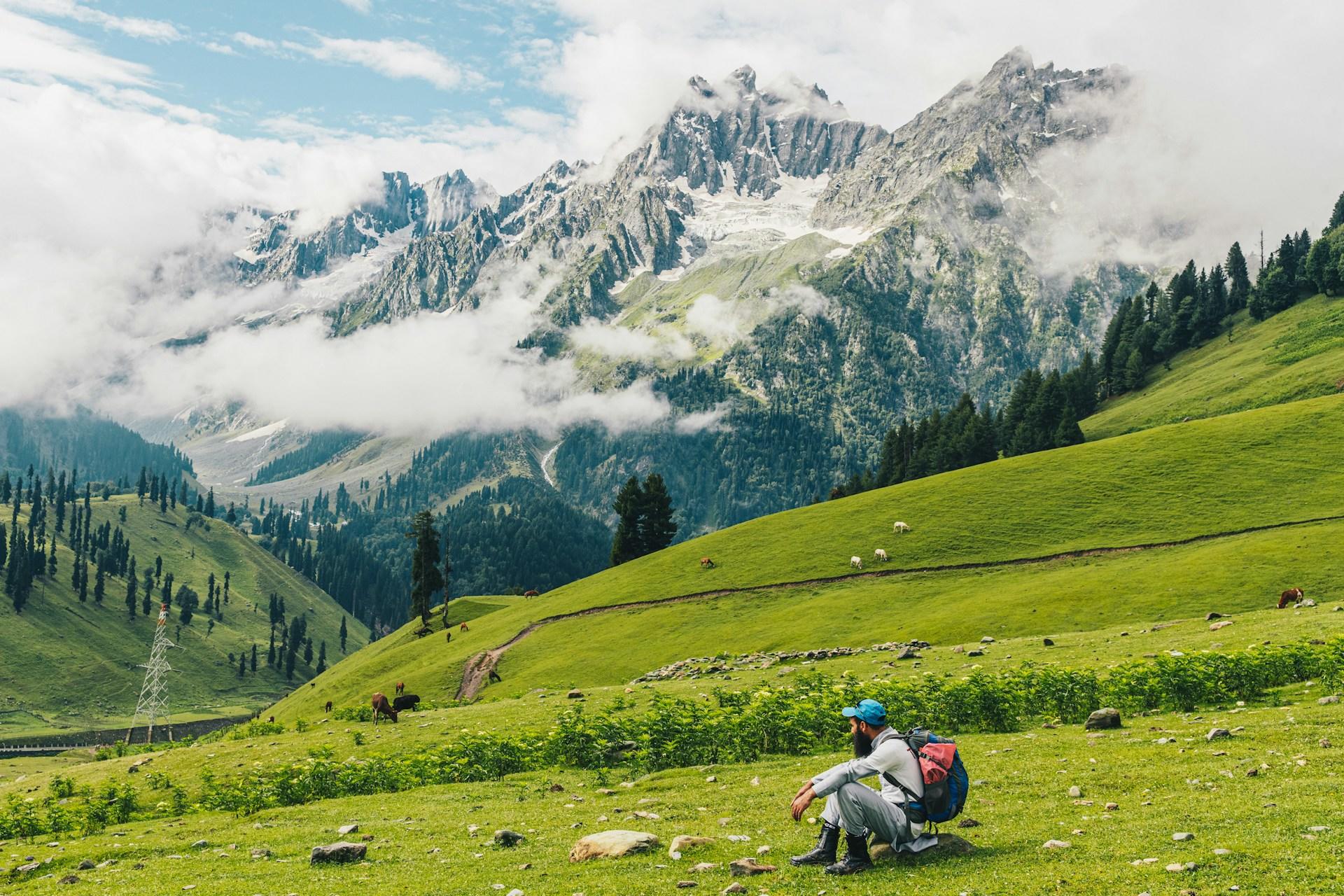Mann sitzt auf grüner Wiese in Gebirge.