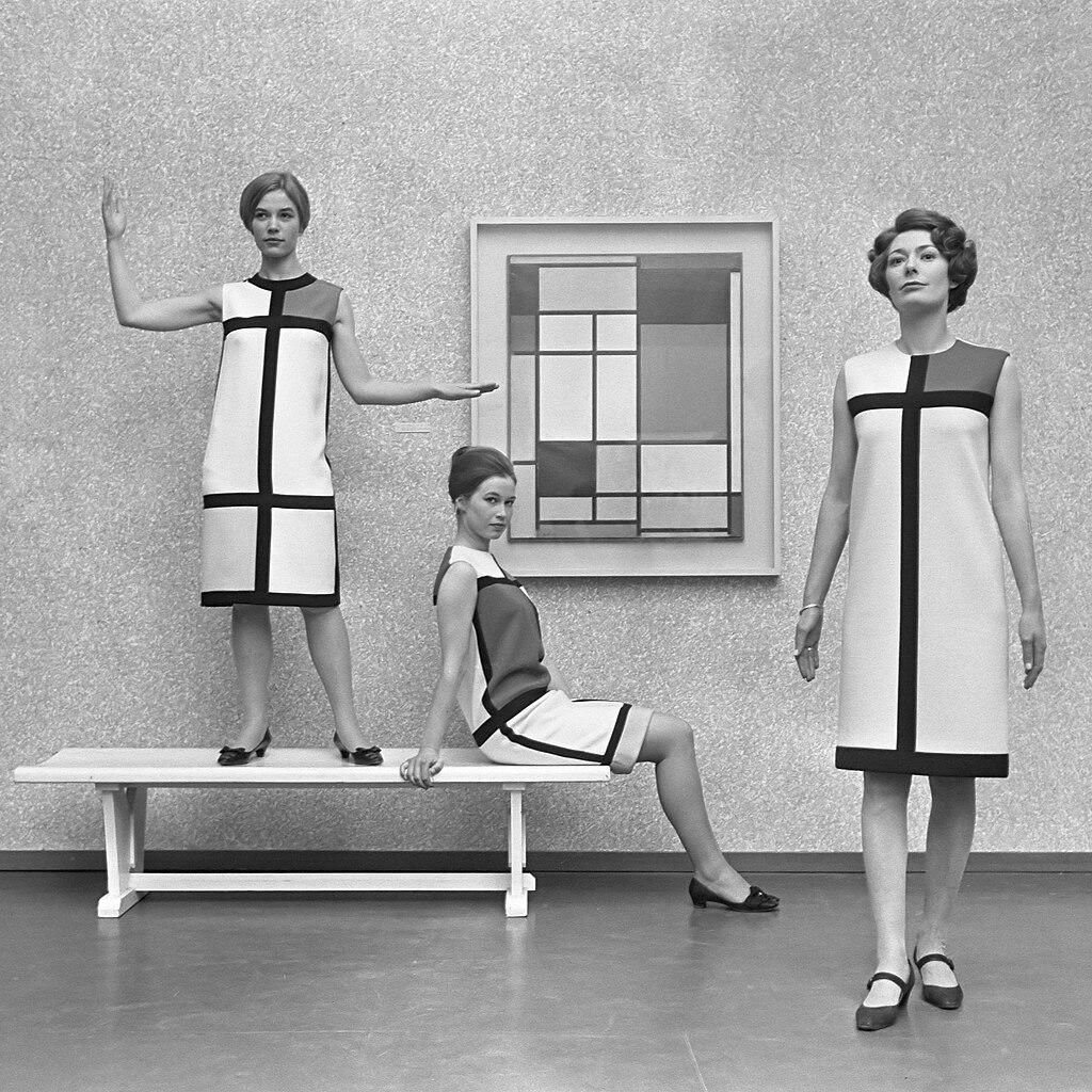 Drei Mannequins in Kleidern mit grafischem Muster vor einem Gemälde mit demselben Muster
