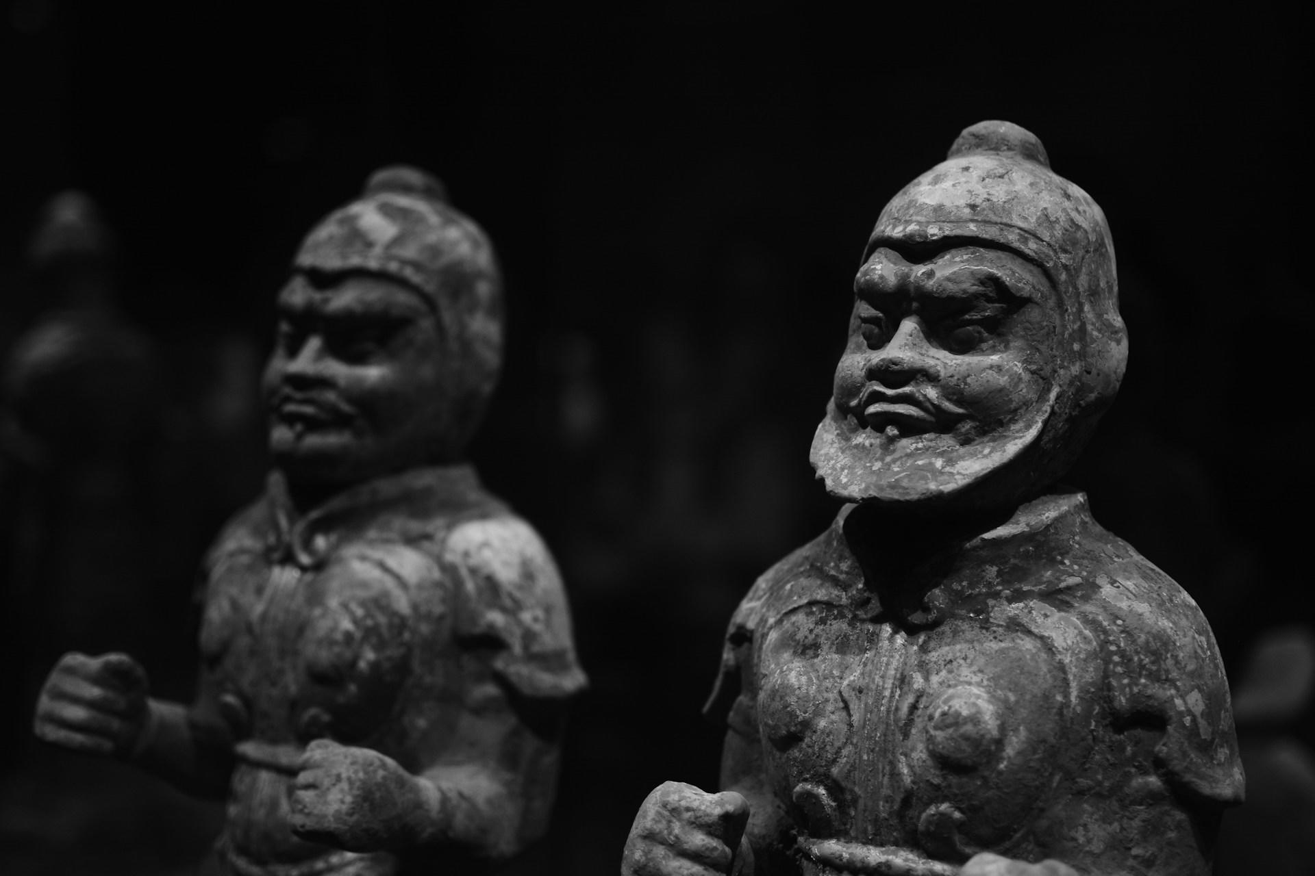 Zwei Bronzestatuen vor dunklem Hintergrund.