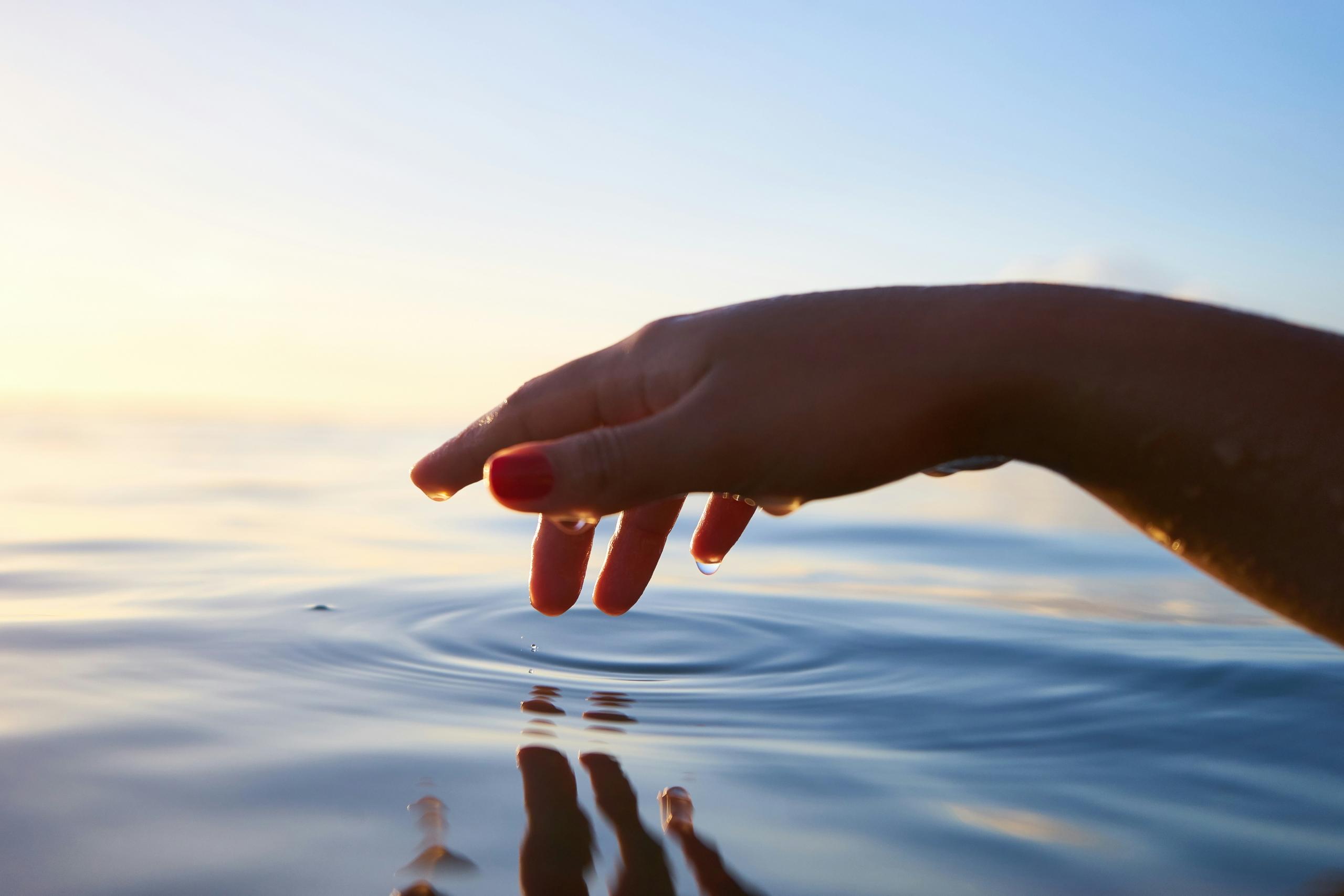 EIne Hand berührt die Wasseroberfläche eines Sees.