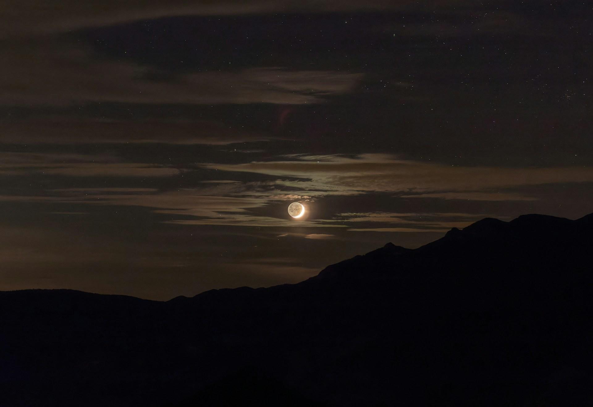Der Vollmond hinter Schleierwolken über einem Hügel