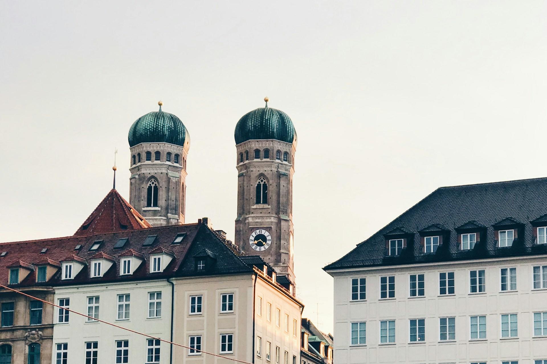 Kirche mit zwei Türmen hinter Häusern.