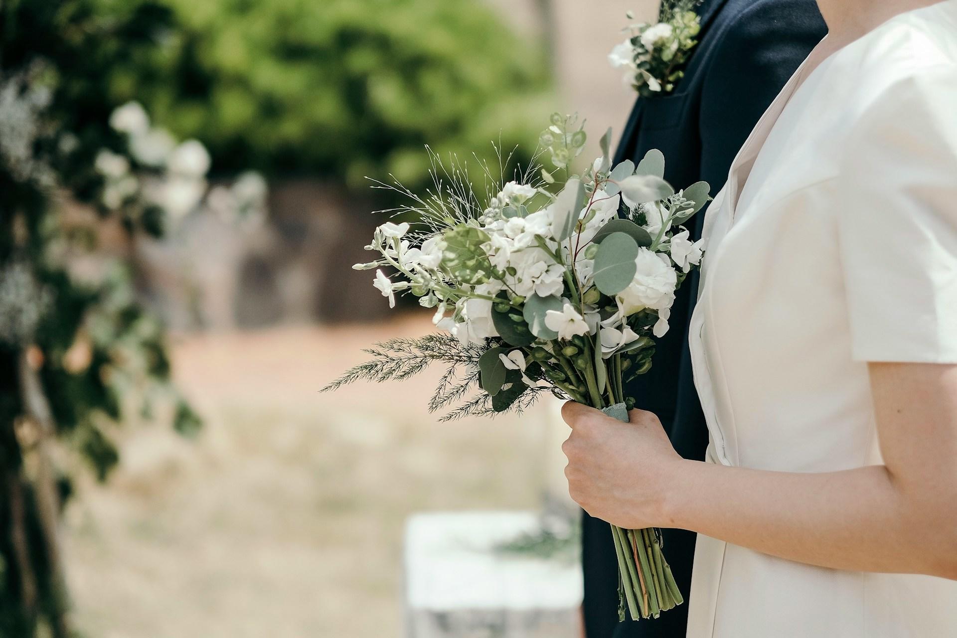 Eine weiß gekleidete Person hält einen Strauß aus weißen Blumen