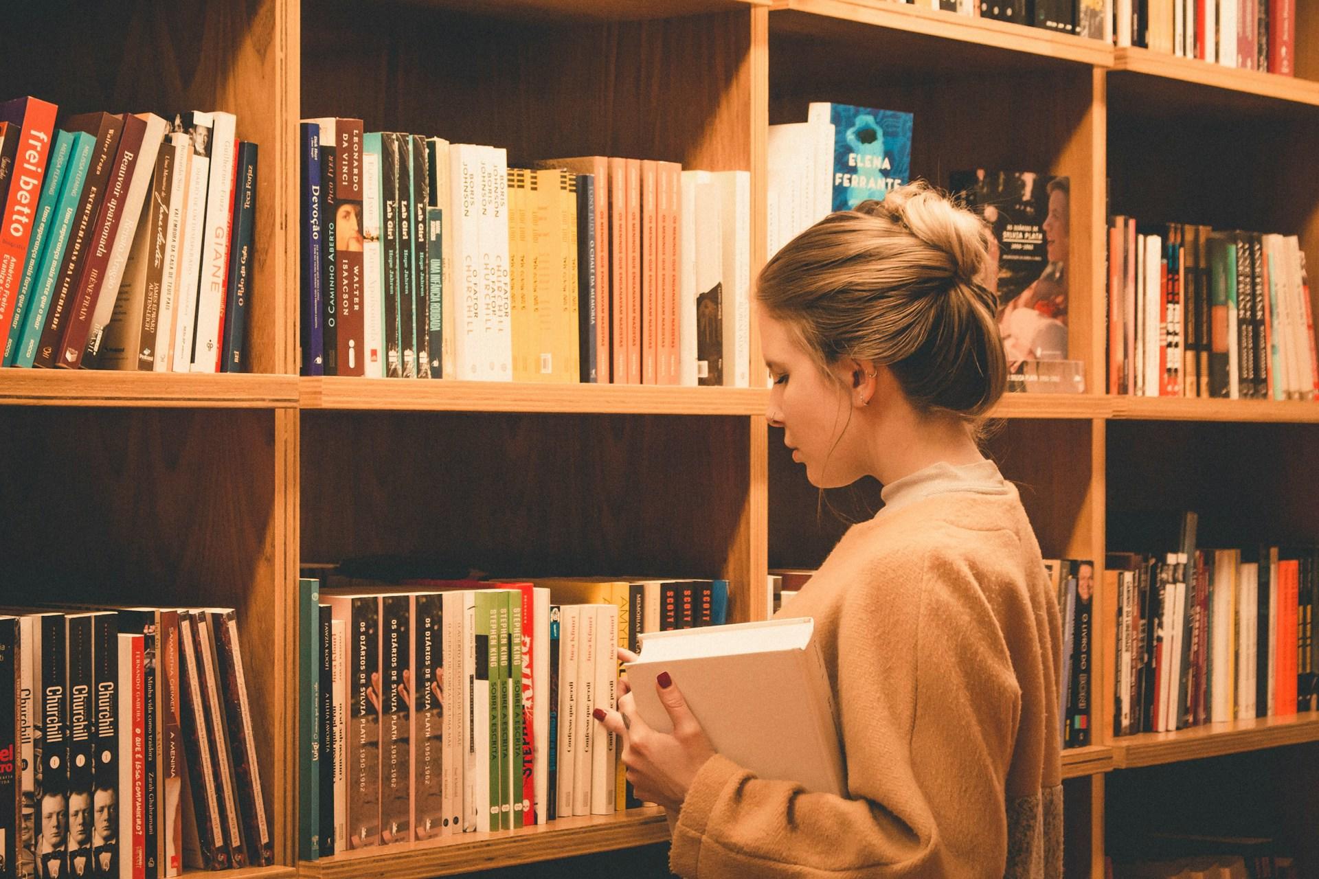 Frau mit Buch in der Hand vor Bücherregal.