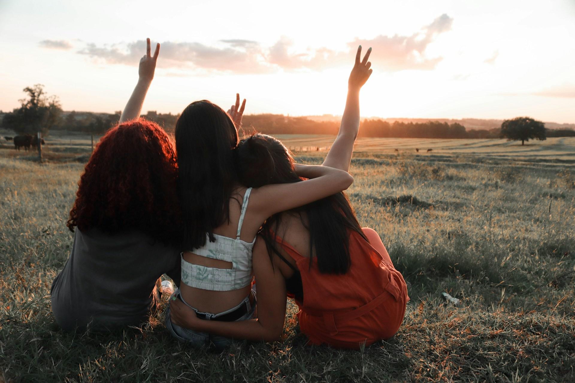 Drei Frauen sitzen auf einer Wiese und halten sich gegenseitig.