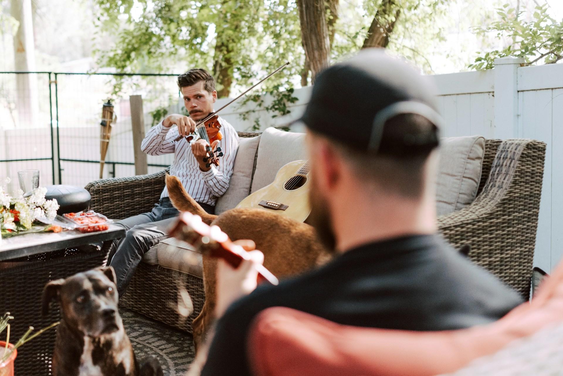 Ein Mann spielt Geige auf einem Sofa und daneben liegt eine Gitarre