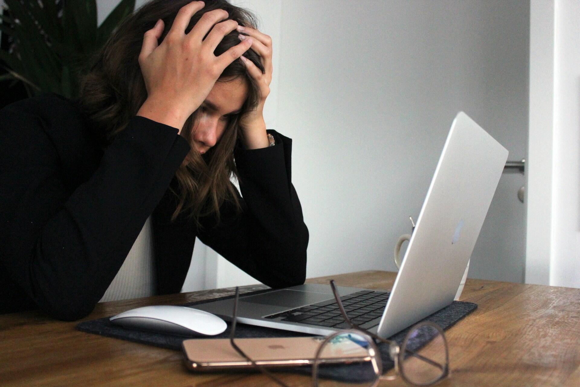 Frau sitzt ohne Motivation am Laptop mit ihren Haenden am Kopf