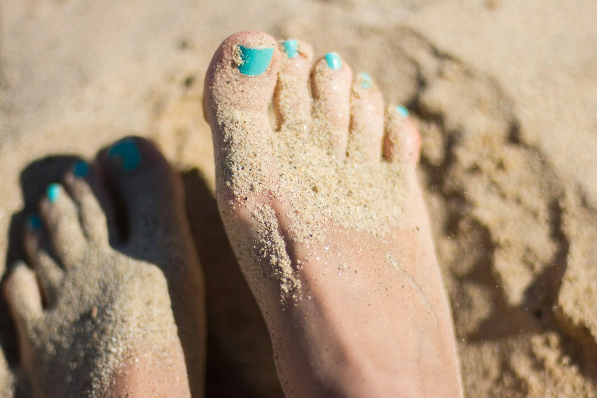 Frauenfüße mit türkis lackierten Nägeln im Sand.