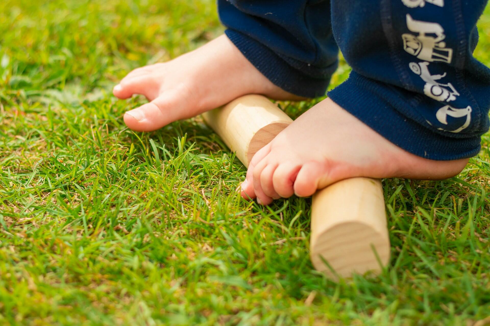 Kinderfüße balancieren auf zwei Holzrollen.