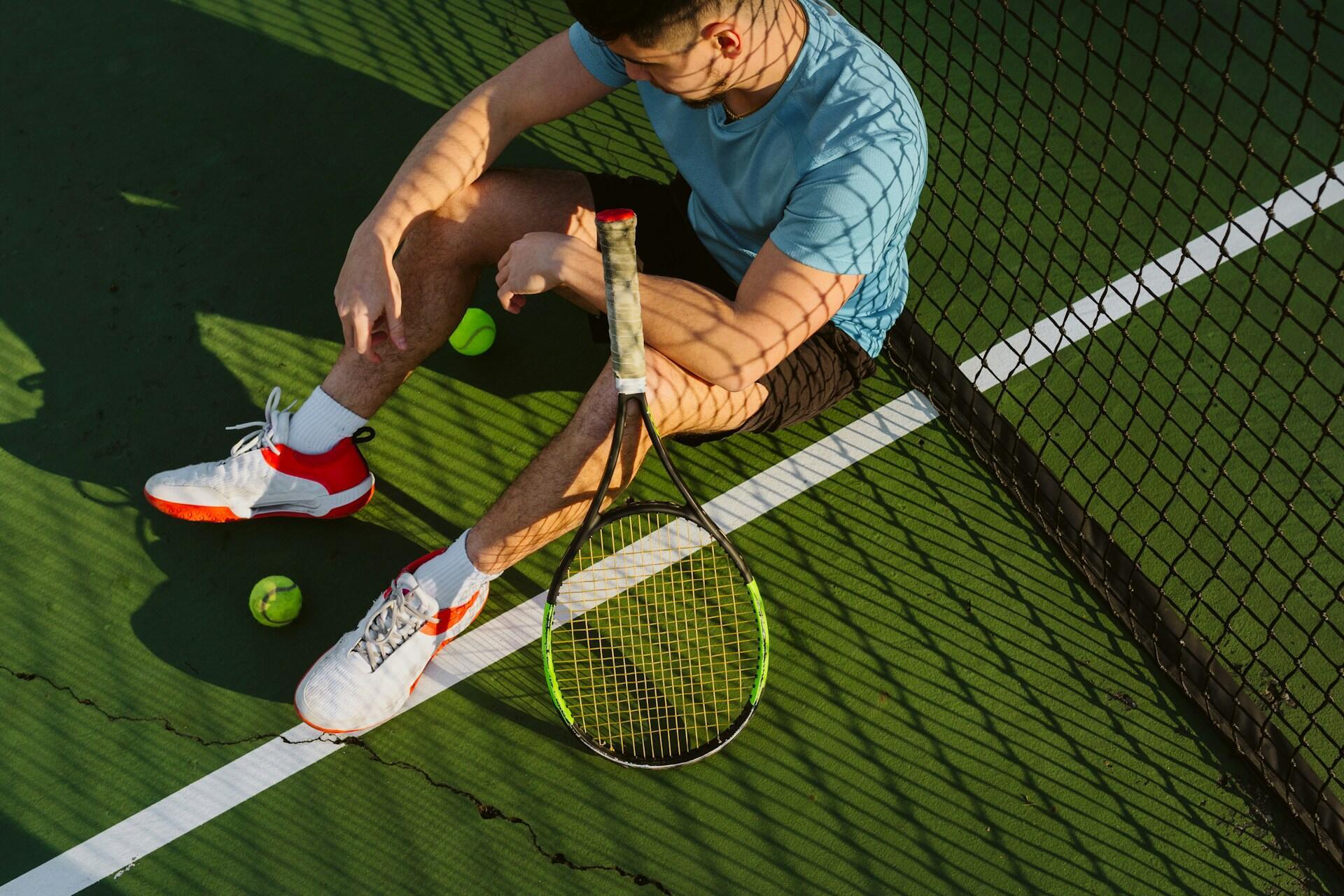 Ein Tennisspieler sitz ans Netz gelehnt auf dem Boden
