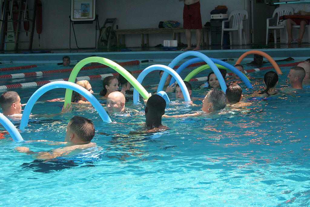 Männer und Frauen trainieren Aquagymnastik mit Schwimmnudeln.