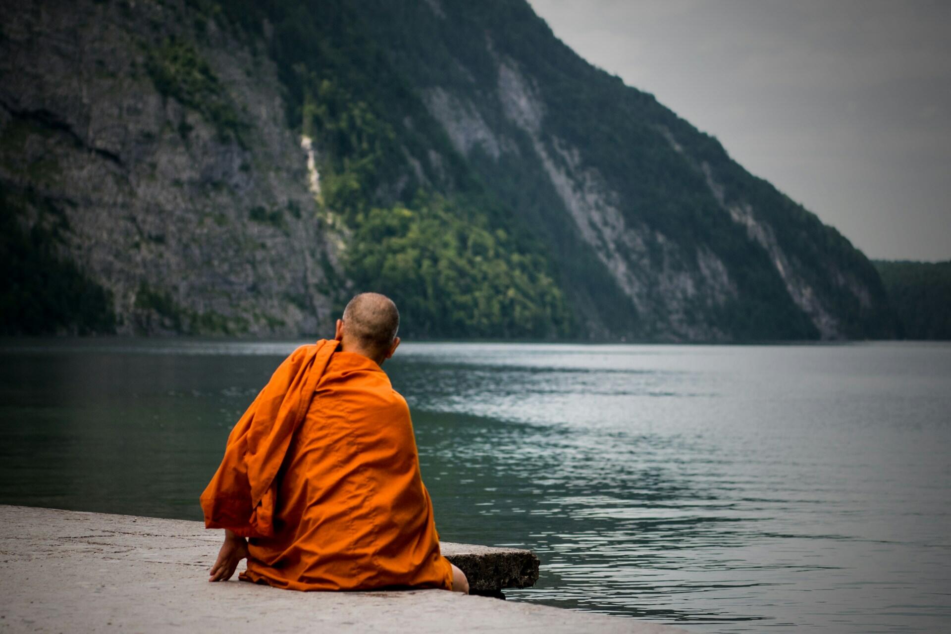Ein buddhistischer Mönch sitzt an einem See und schaut aufs Wasser.