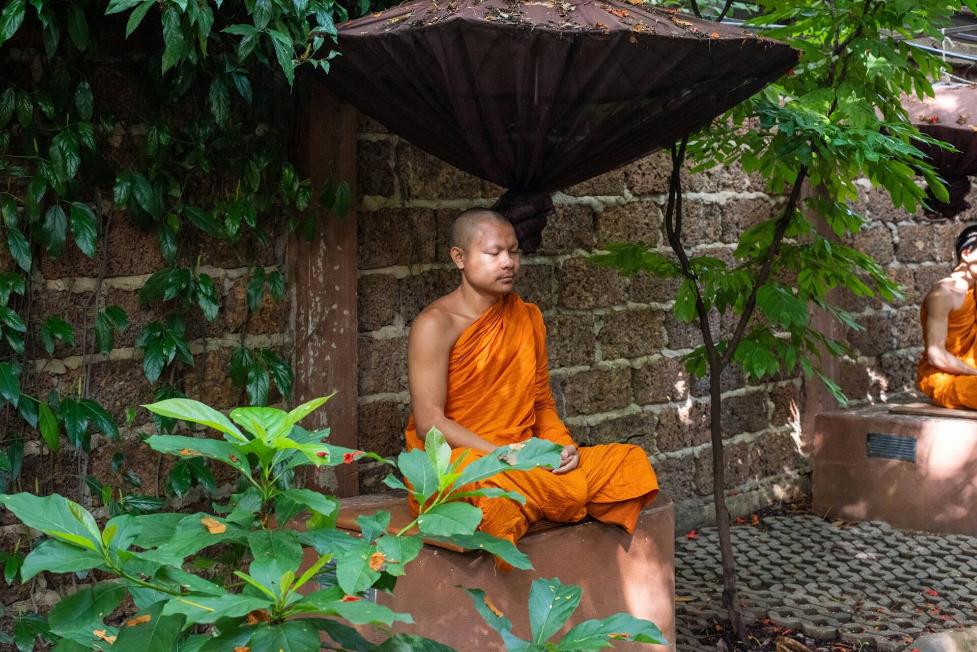 Ein Buddhistischer Mönch in orangener Robe sitzt im Schneidersitz auf einem Stein.