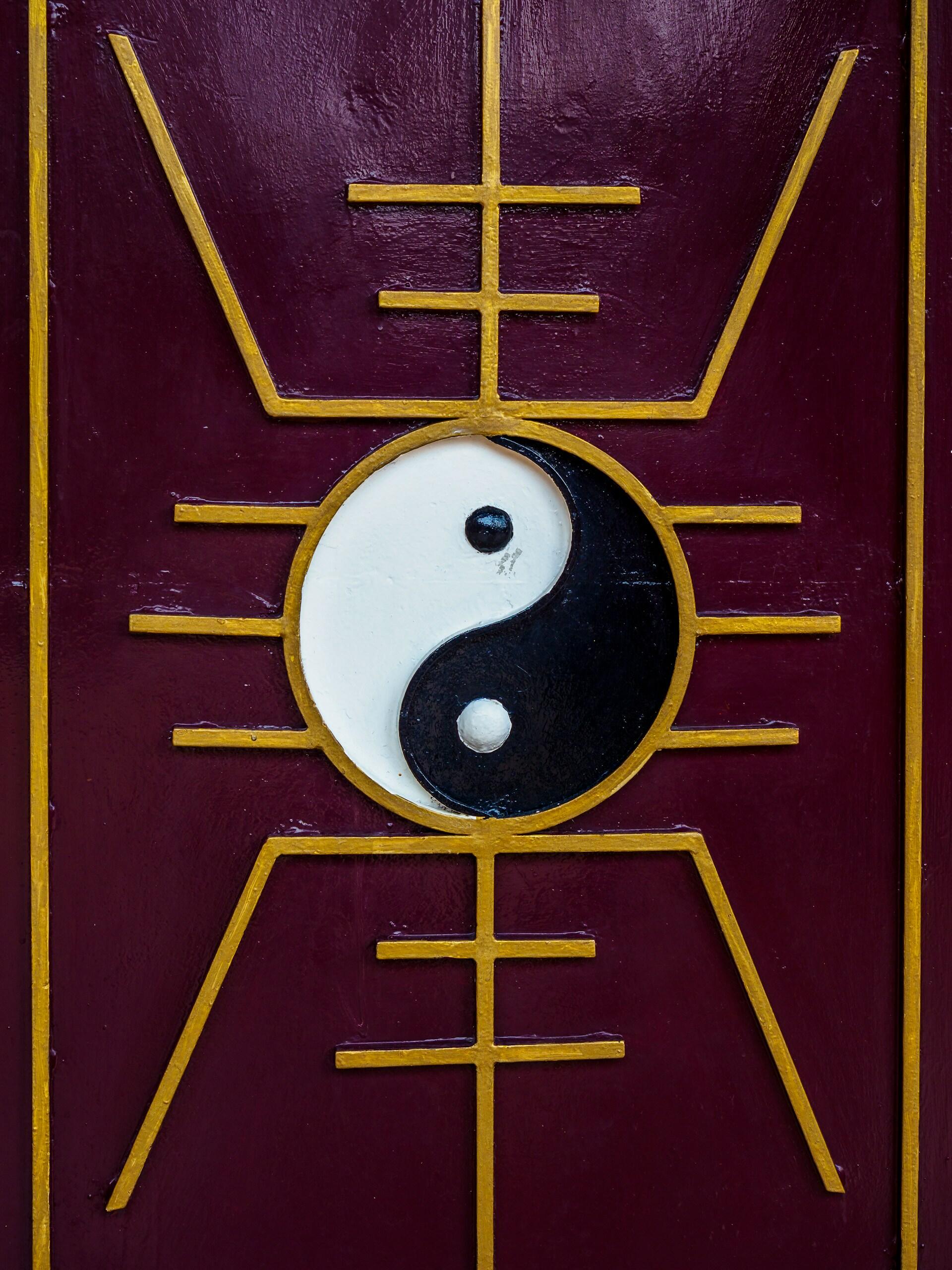 Ein Ying und Yang Zeichen auf einer dunkelroten Holzvertäfelung mit goldenen Elementen.