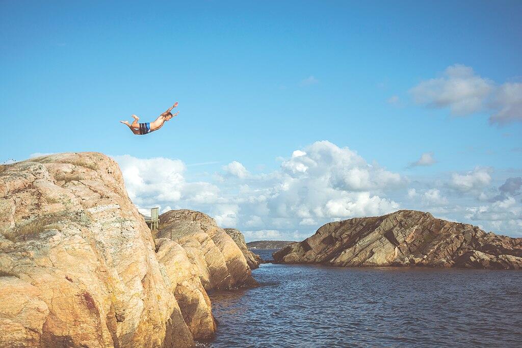 Ein Mann Springt von einer Klippe und sieht aus als wolle er einen Bauchplatscher machen.