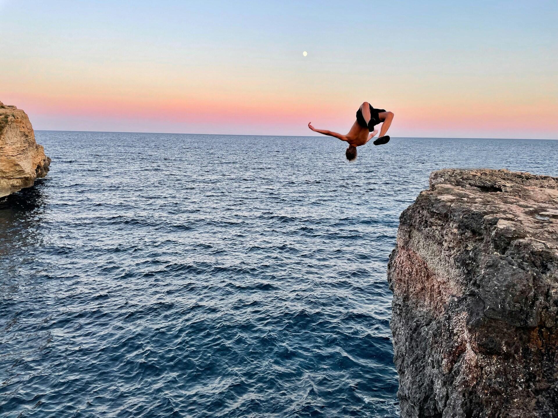 Ein Mann springt mit einem Salto im Sonnenuntergang von einer Klippe.