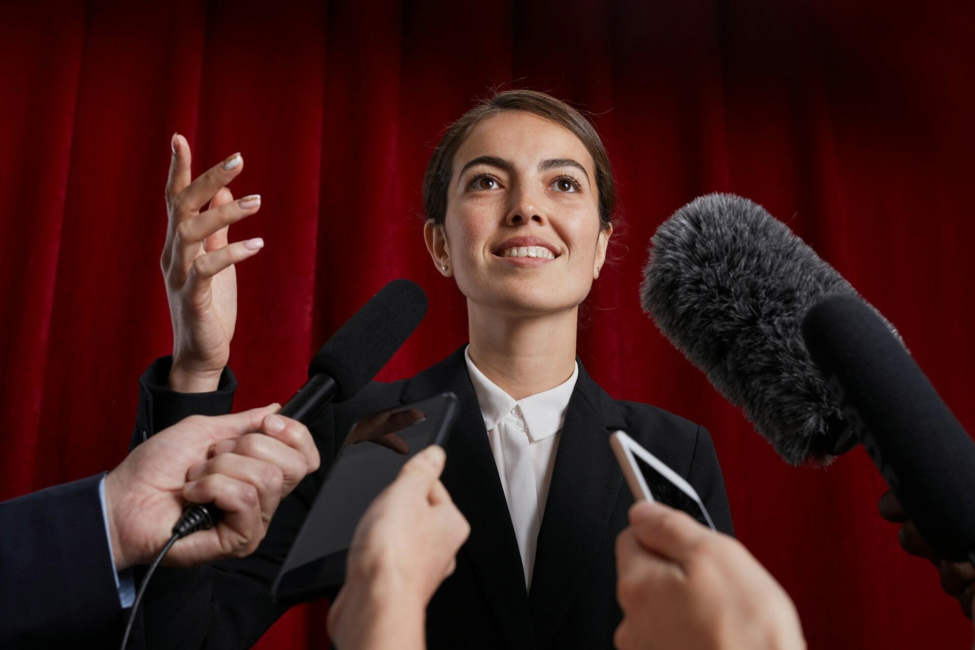 Mikrofone und Handys werden einer selbstbewusst lächelnden Person entgegen getstreckt