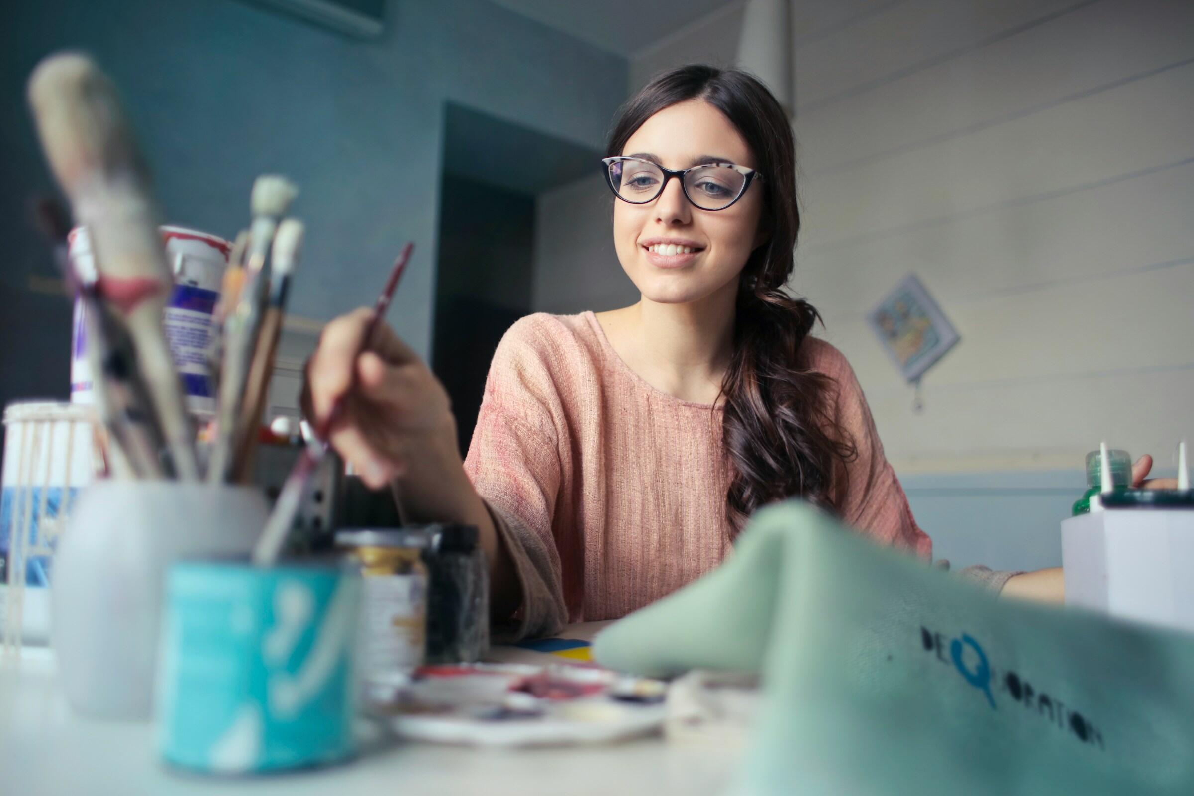 Eine junge Frau mit Brille malt ein Bild und wäscht grade ihren Pinsel aus.
