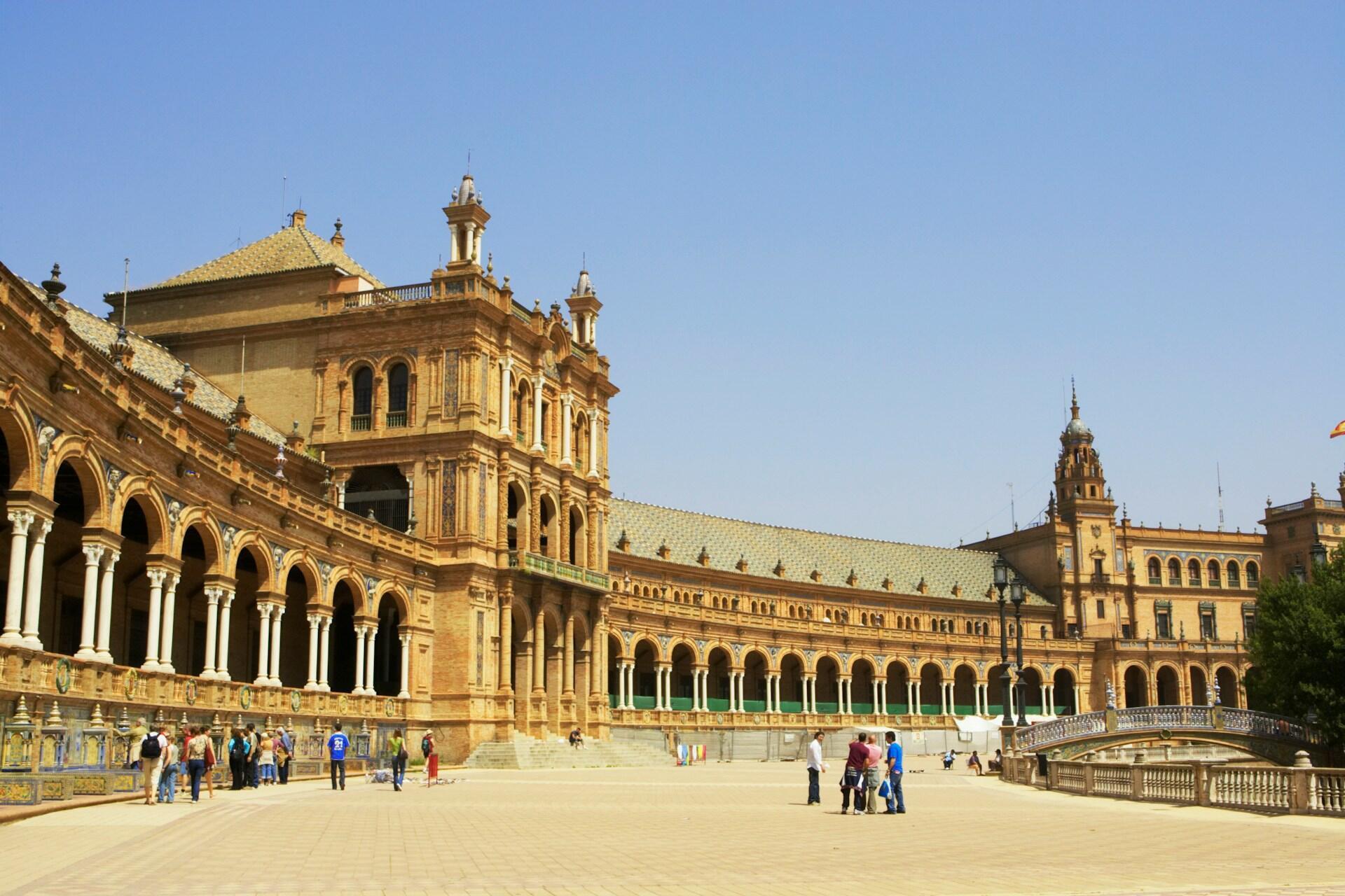 Der Plaza de España in Sevilla mit seiner beeindruckenden Backsteinarchitektur seinen Bögen und Besuchern auf dem Platz davor.