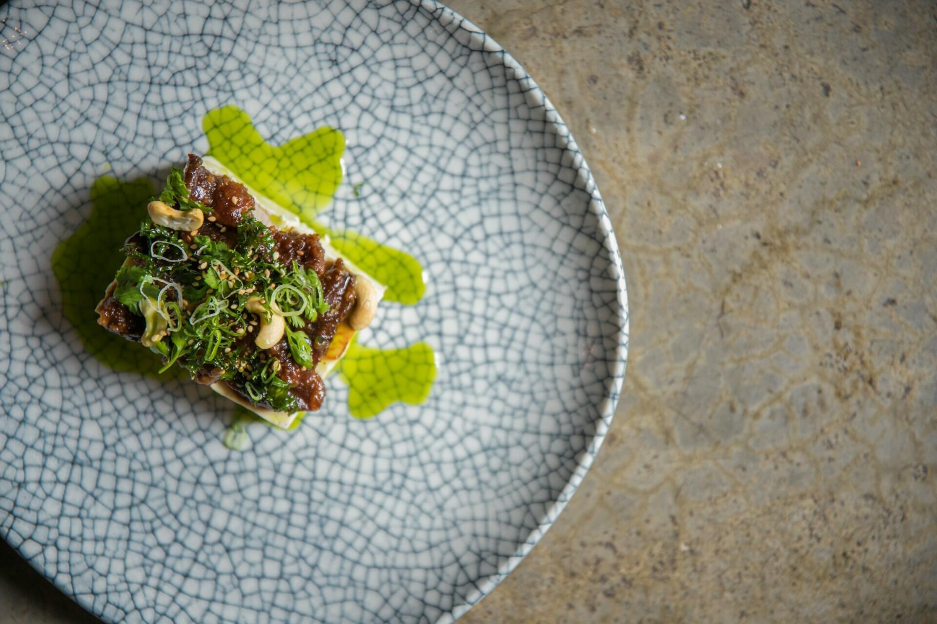 Ein sorgfältig angerichteter Teller mit köstlichen Zutaten, aromatischen Kräutern und Cashewkernen auf einem weißen Teller mit Struktur und einem Hauch grüner Sauce.