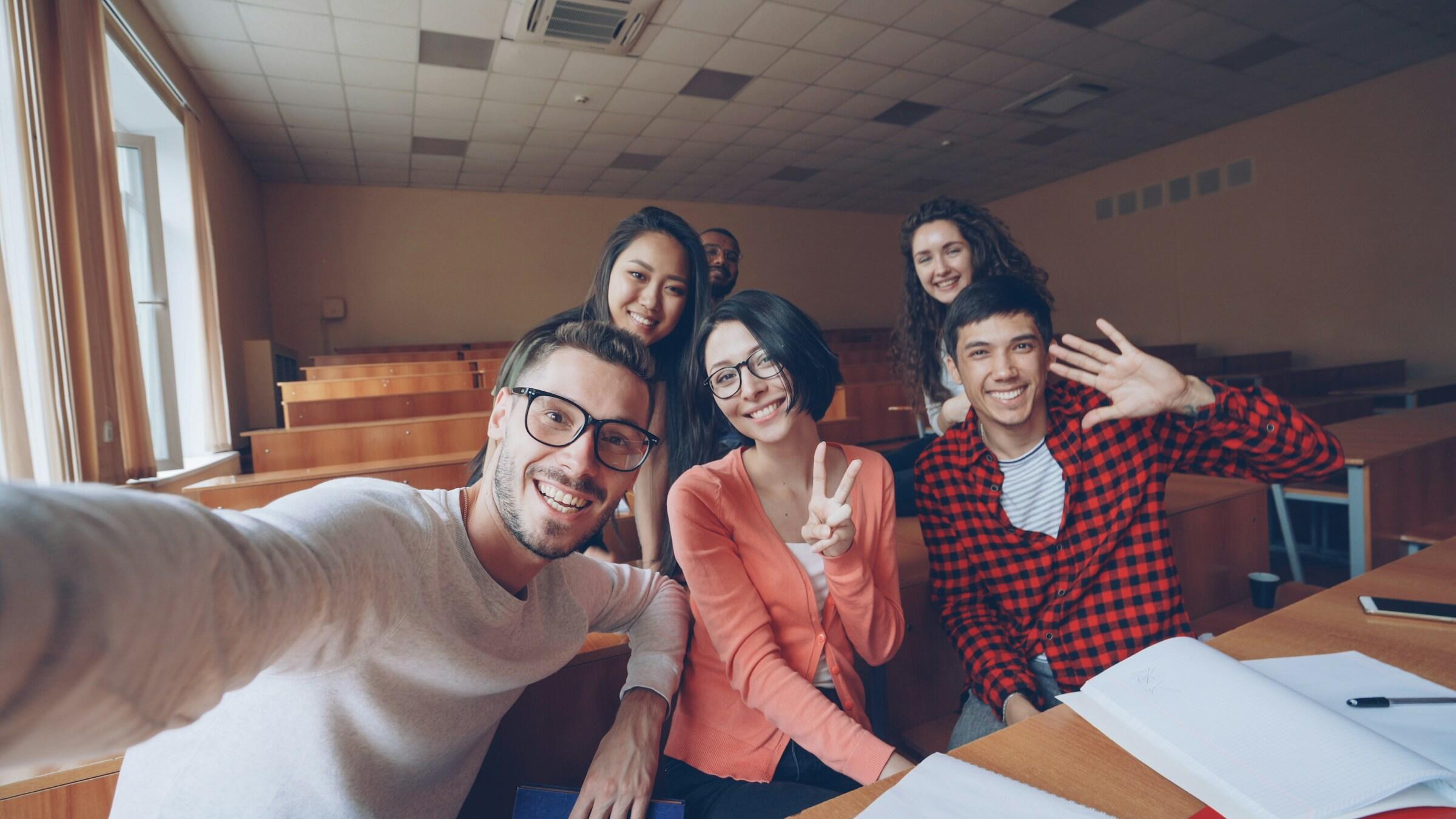 Eine Gruppe junger Leute versammeln sihc im Klassenraum vor er Kamera für ein Selfie.