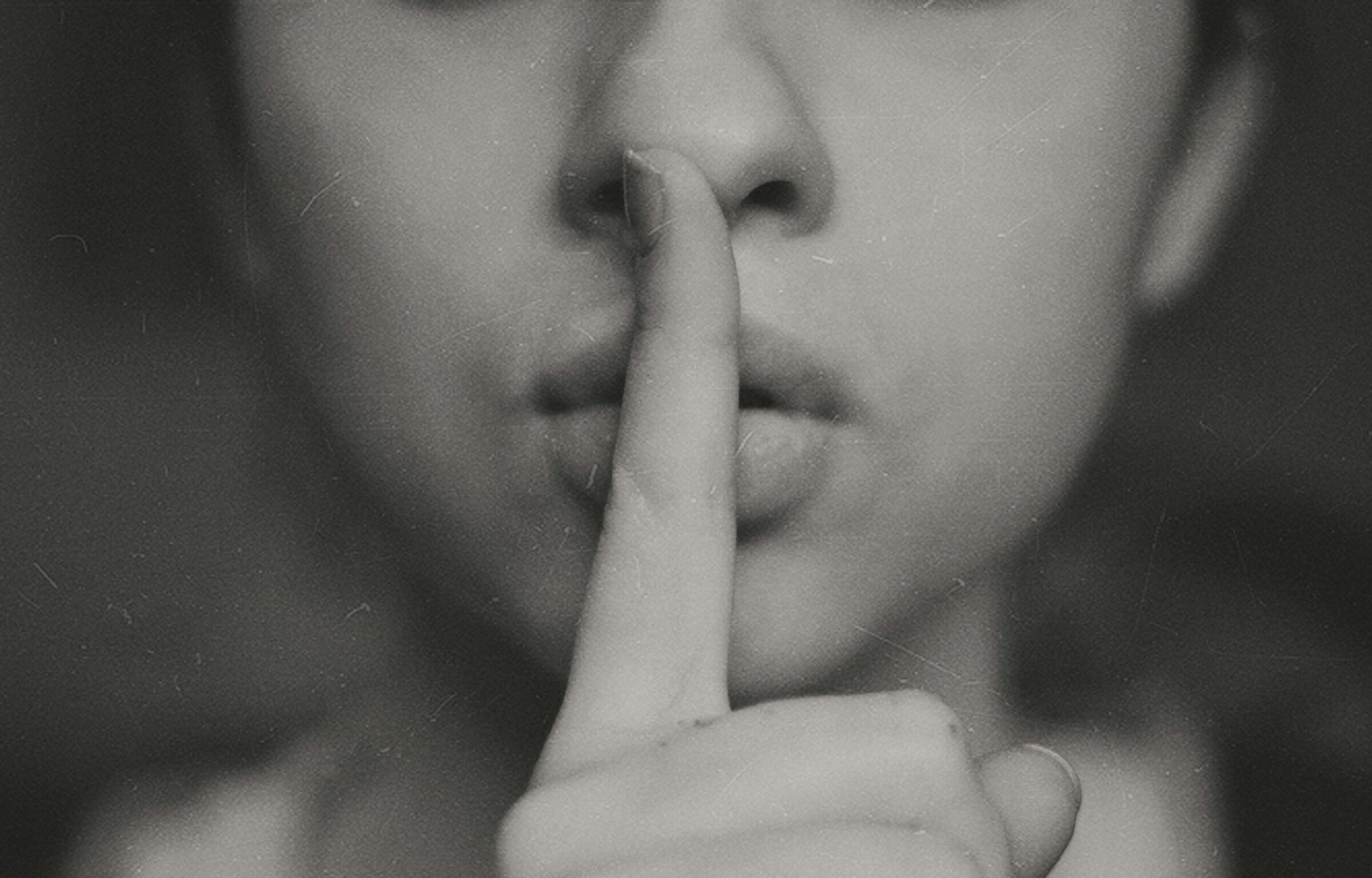 Eine Frau hebt den Finger vor die Lippen.