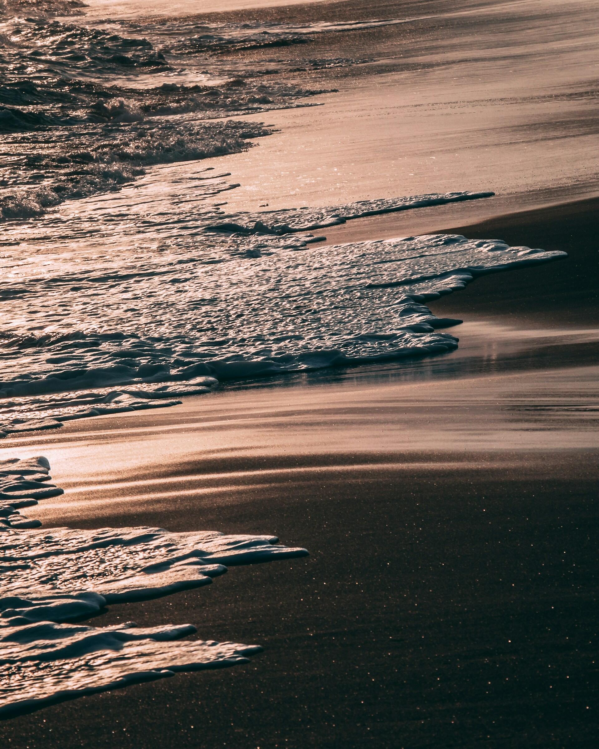 Wellen ziehen sich auf einem Sandstrand zurück.