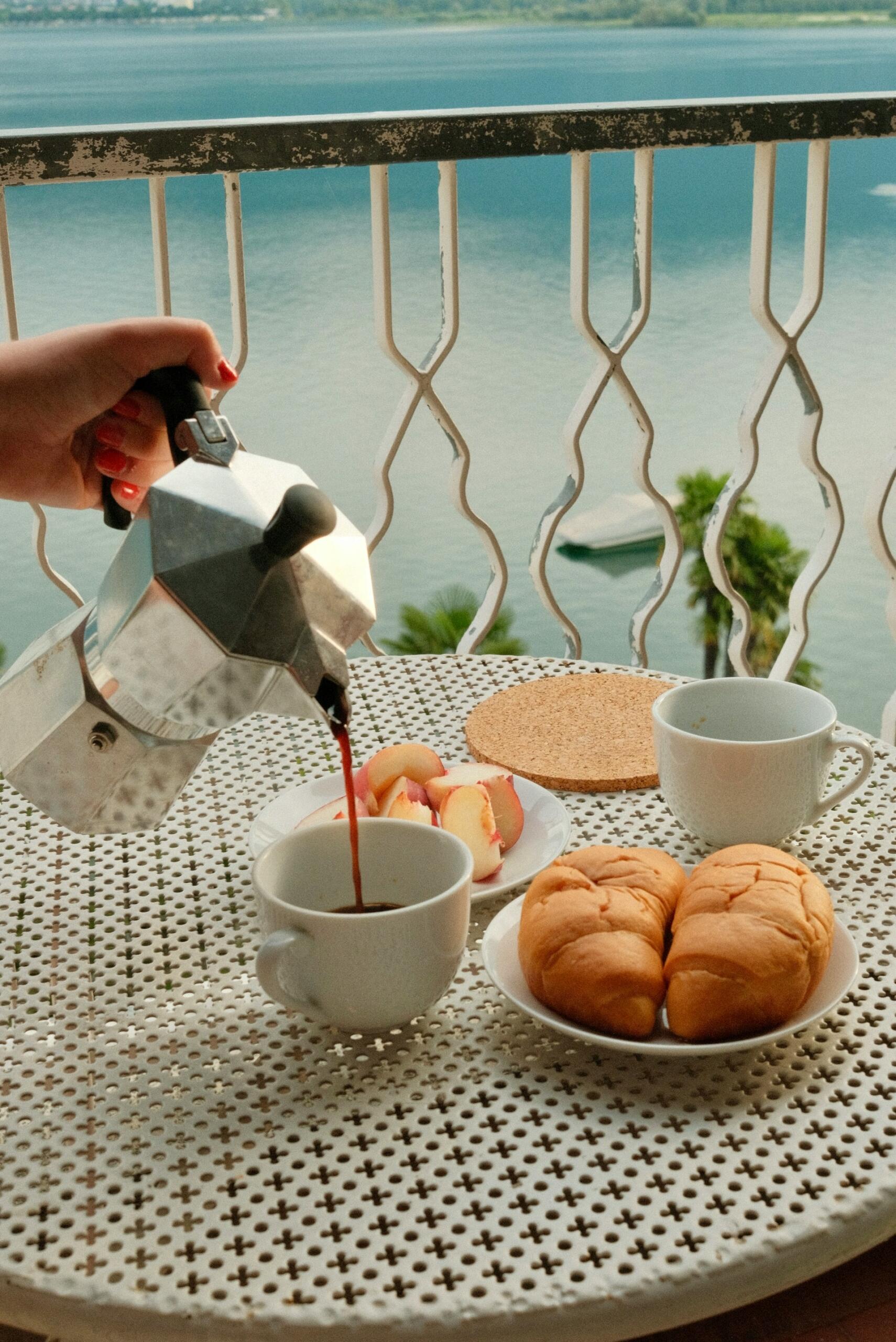 Aus einer Espressokanne wird Kaffee in eine Tasse auf einen gedeckten Tisch mit Gebäck gegossen