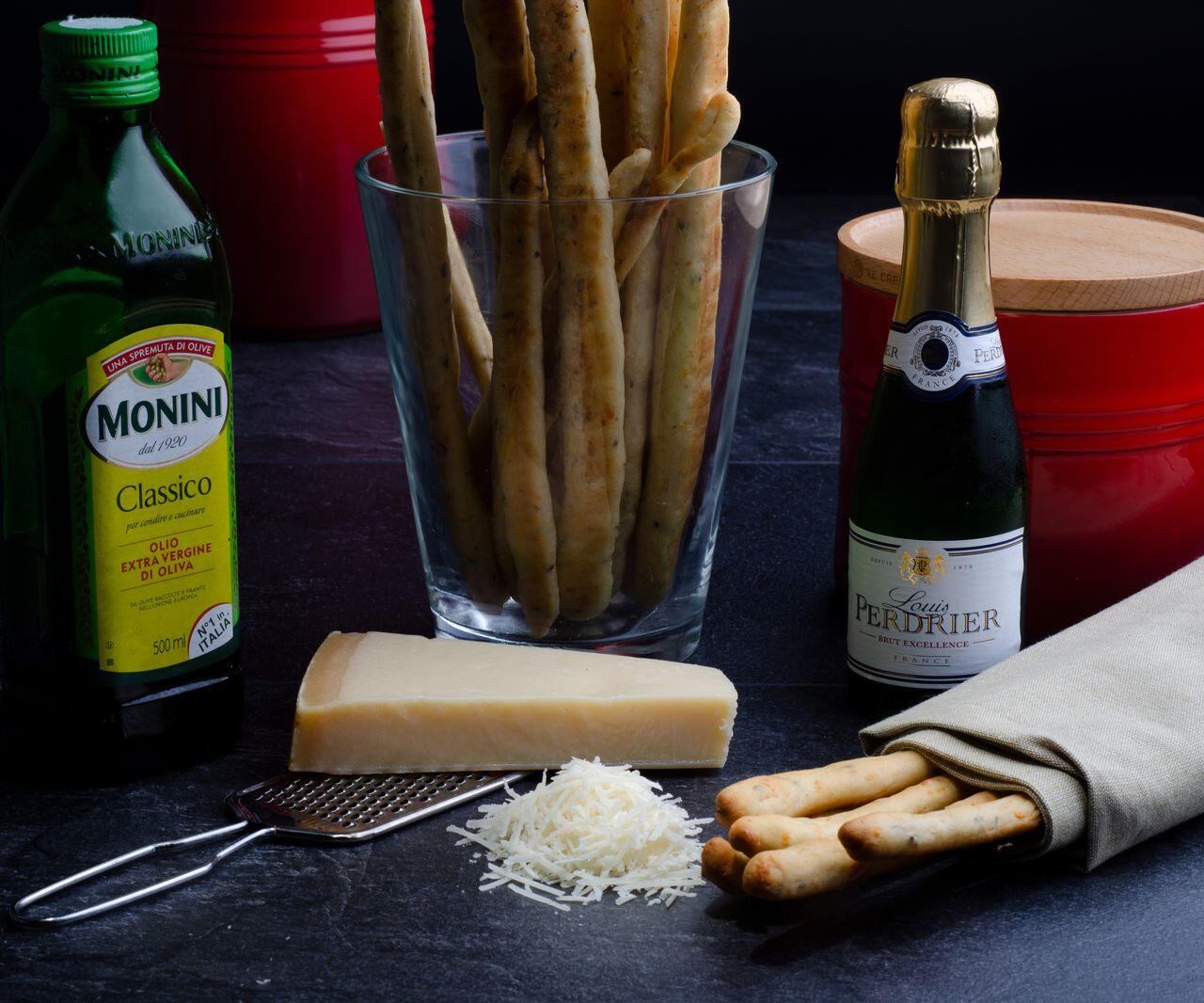 Grissini neben Öl, Champganer und Parmesan