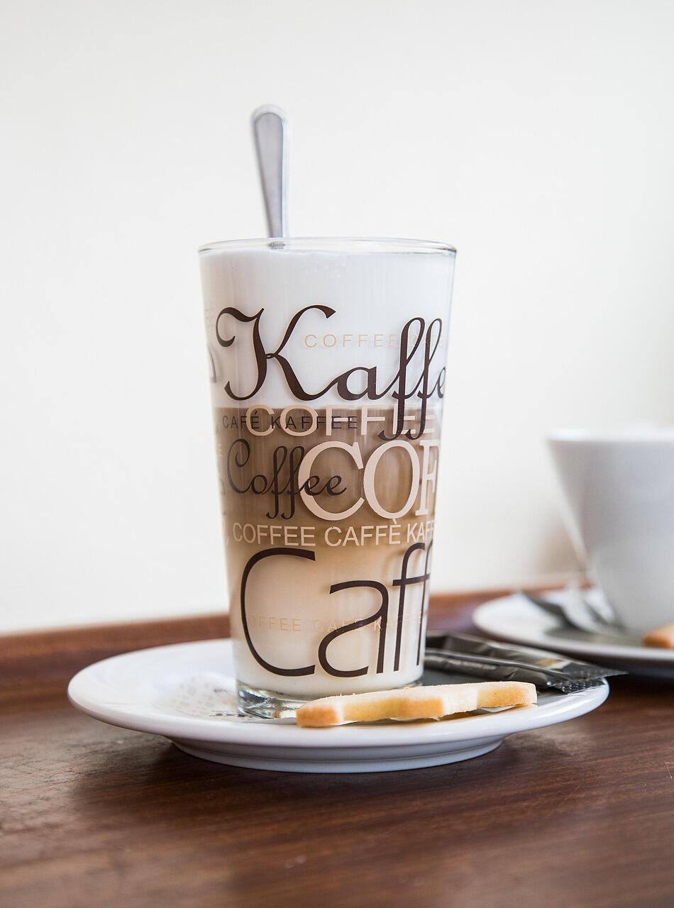 Latte Macchiato in einem hohen Glas auf einem Unterteller mit Keksen