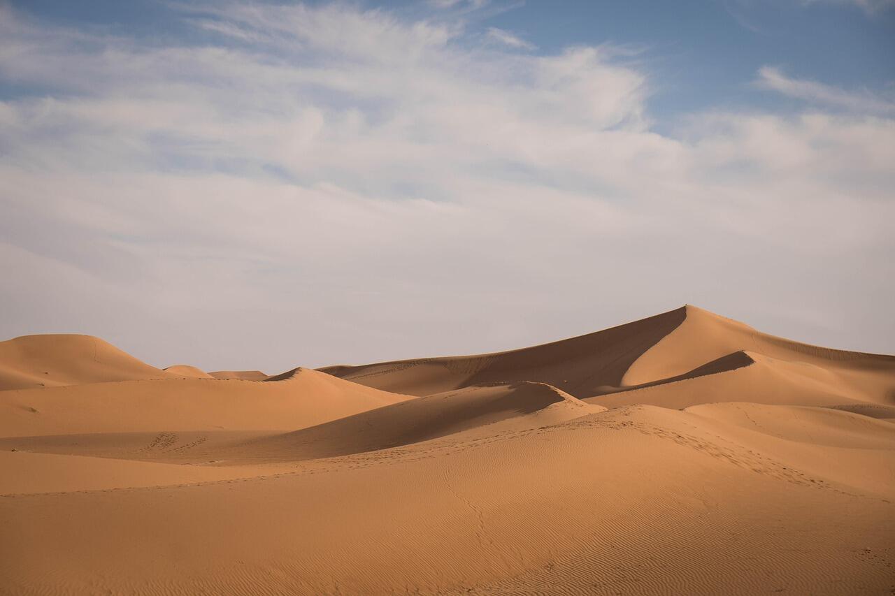 Sandwüste mit Hügeln vor wolkigem Himmel