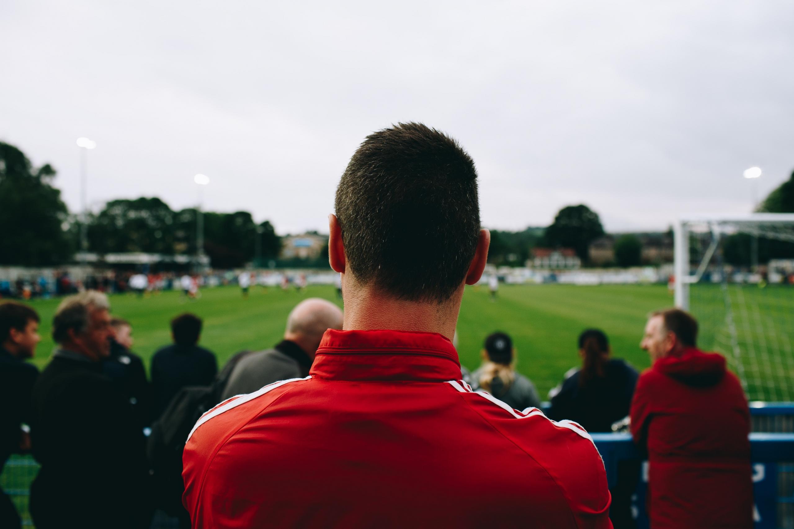 En mand står med ryggen til og ser på danske fodboldspillere spille fodbold