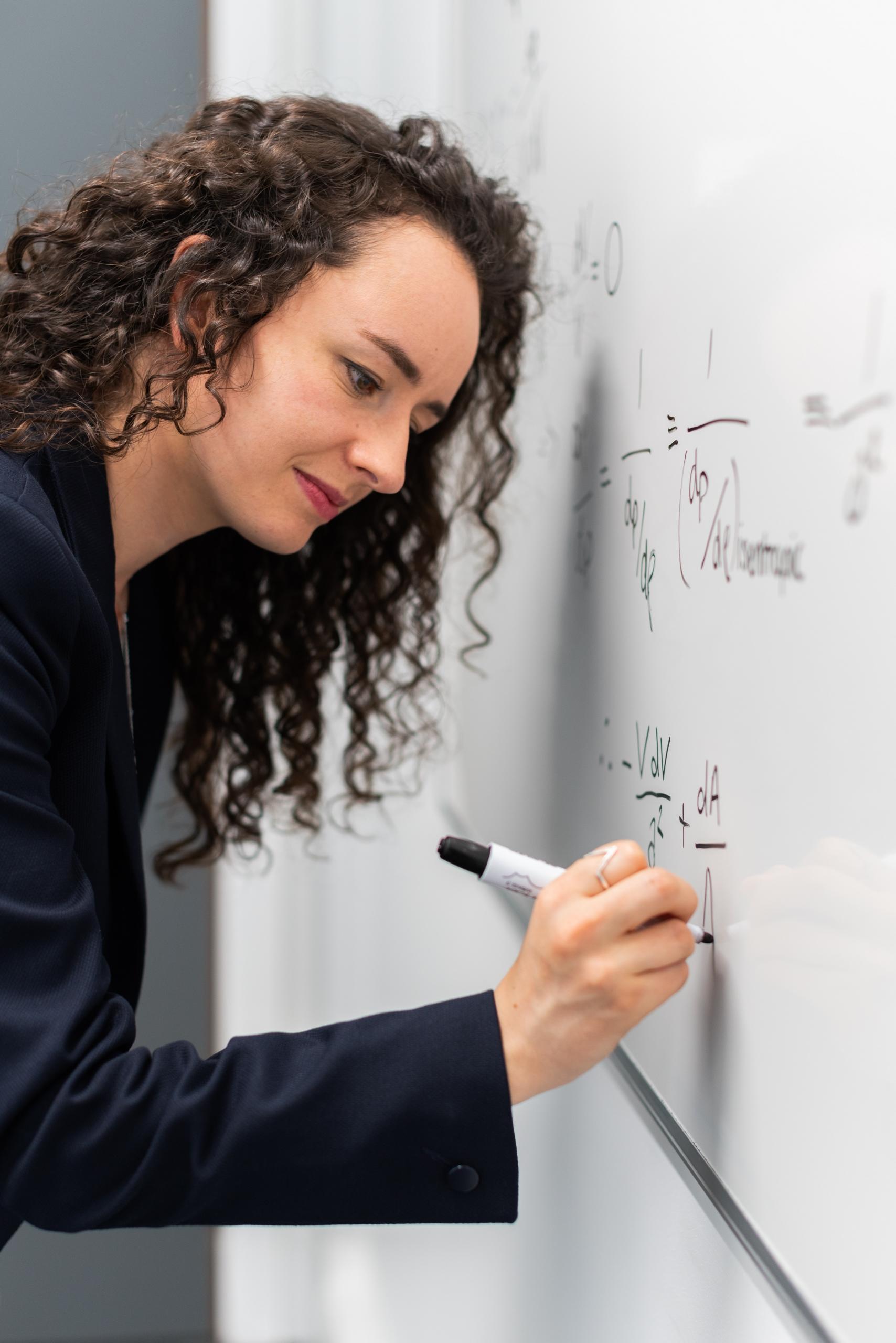 en kvinde skriver på en tavle og underviser i matematik og fysik