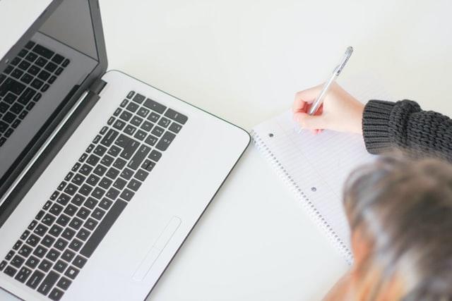 Mädchen mit Computer schreibt auf Block. Nachhilfeunterricht kann in Winterthur auch über den Computer stattfinden!