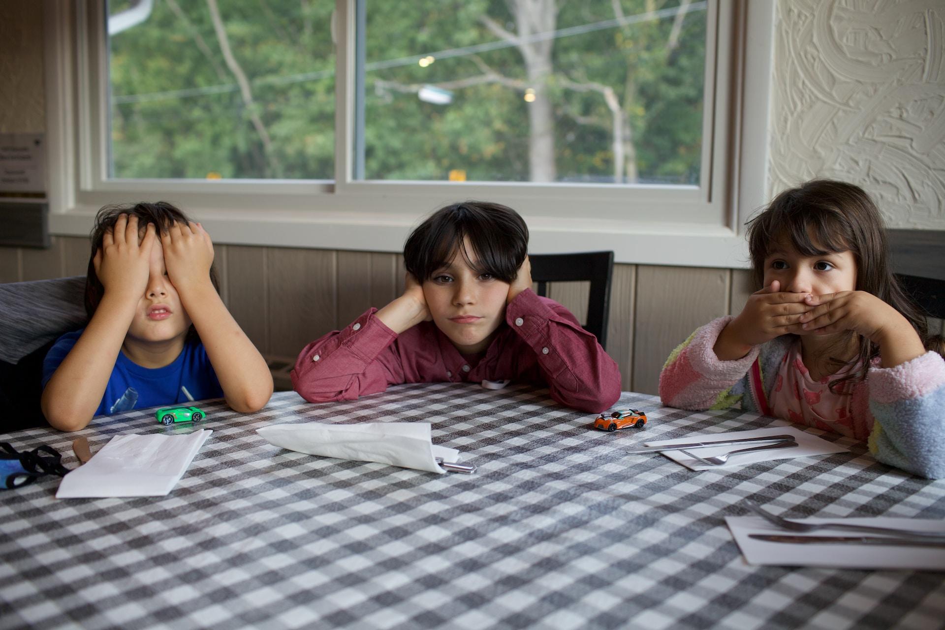 Drei Kinder sitzen an einem runden Tisch.