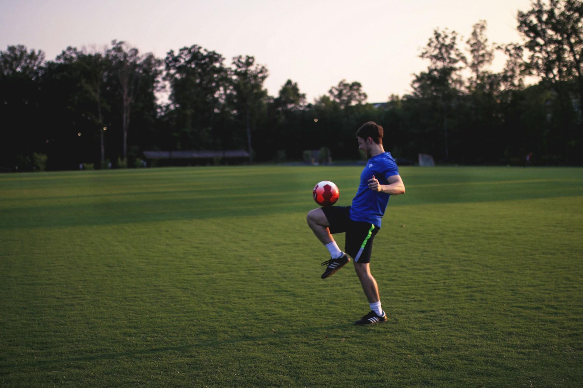 Mann in Sportsachen auf Rasen mit Ball auf Knie.