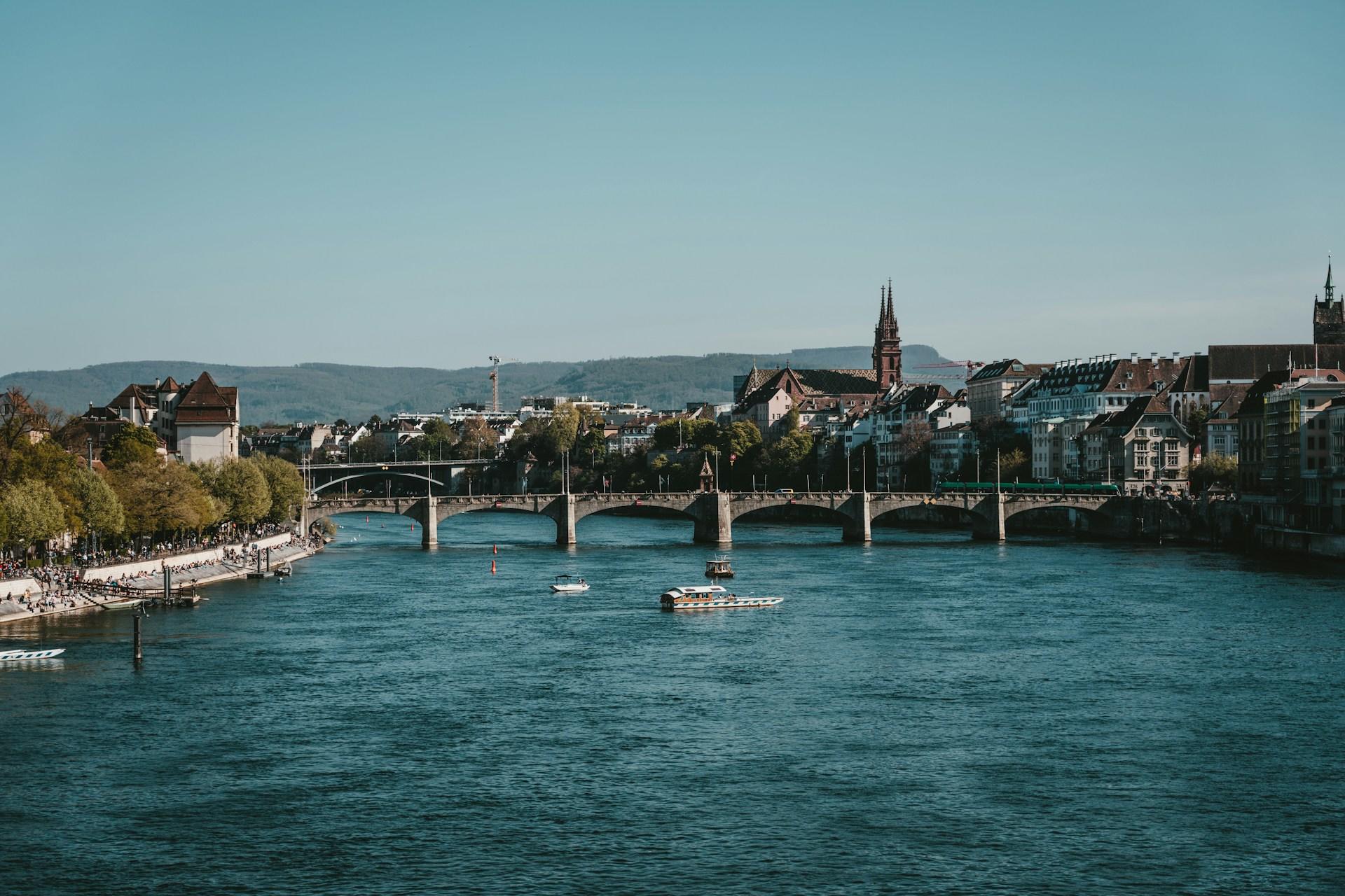 Blick auf Fluss in Basel mit Brücke und Gebäuden.