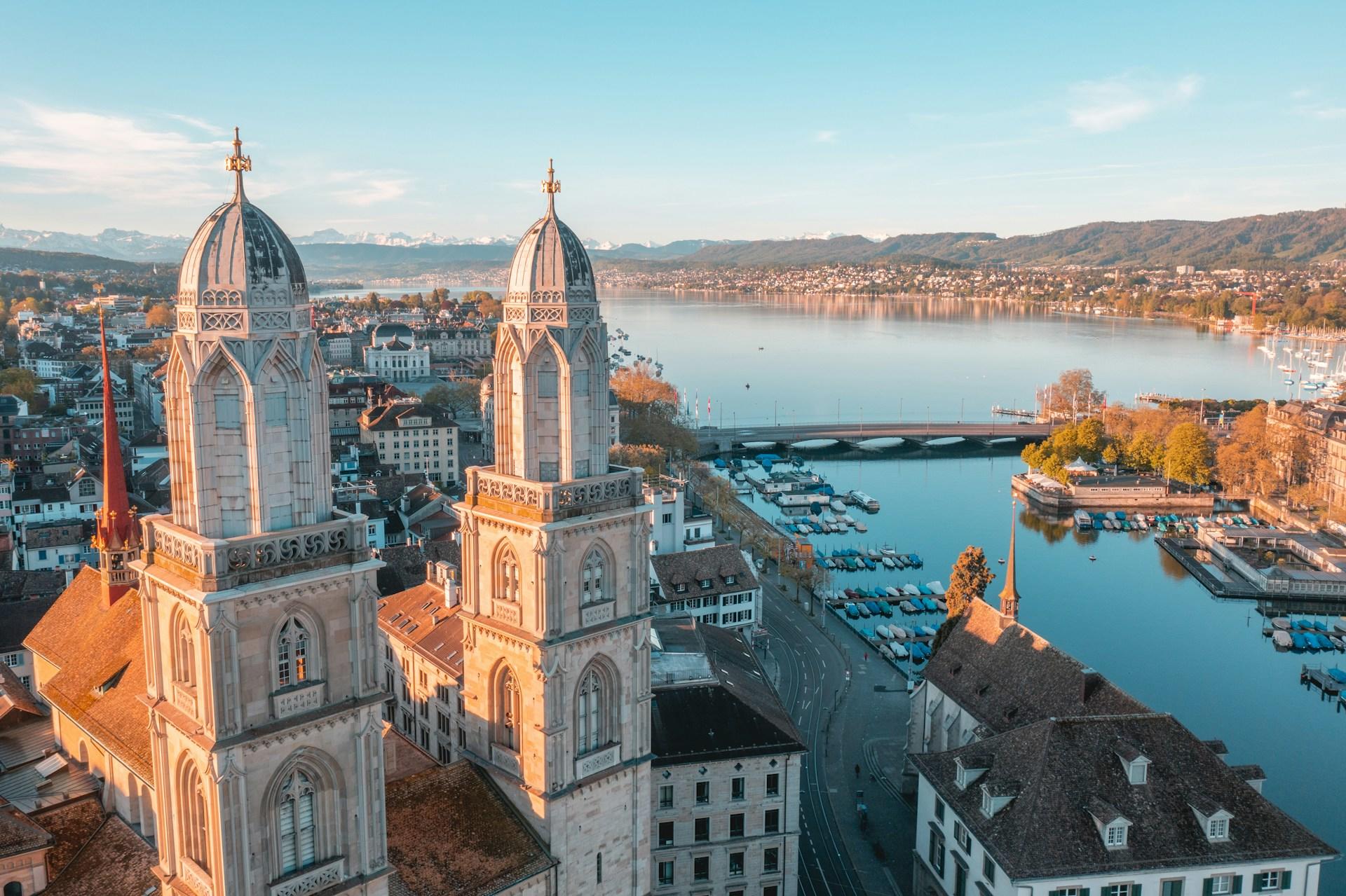Zwei Kirchtürme vor Stadt mit Fluss.