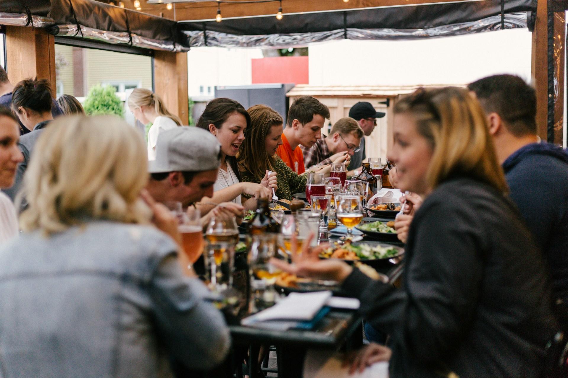 Mehrere Menschen sitzen an langem Tisch mit Essen und Getränken drauf.