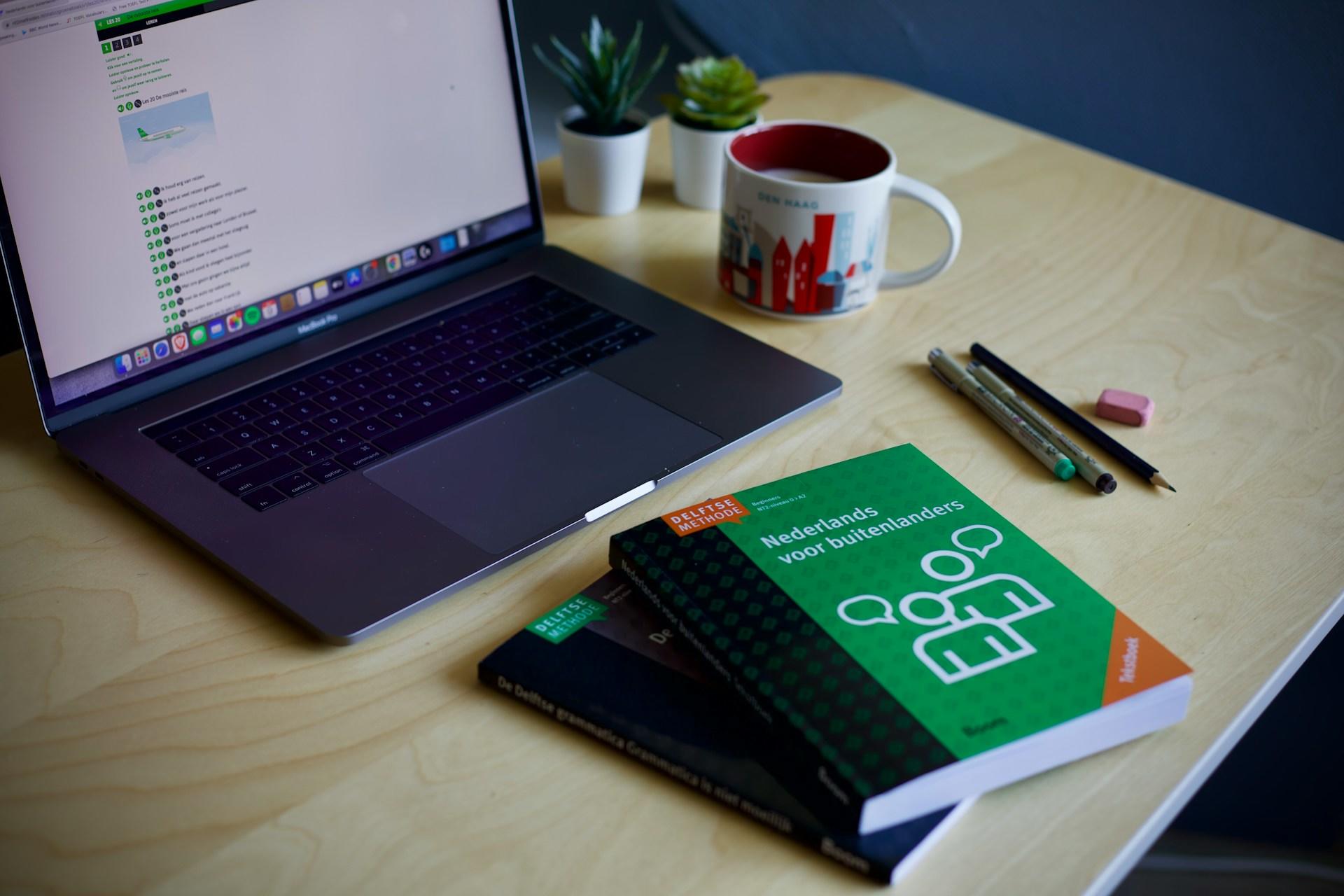 Schreibtisch mit Laptop und Kaffeetasse vor Büchern.