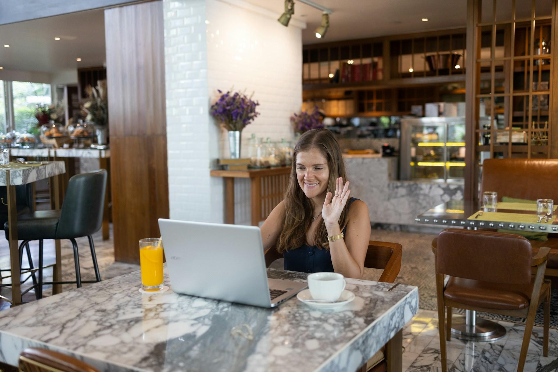 Frau sitzt in Café am Tisch vor Laptop.