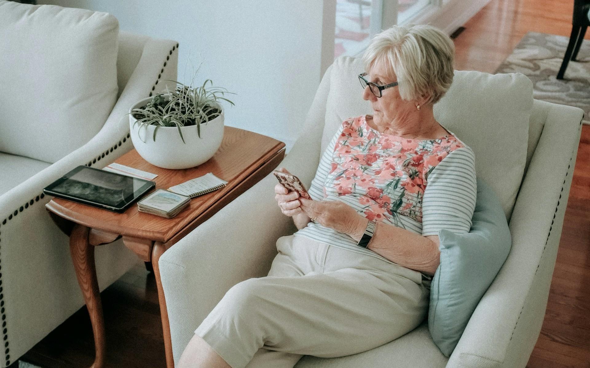 Eine ältere Dame sitzt auf einem Sessel mit dem Smartphone in der Hand