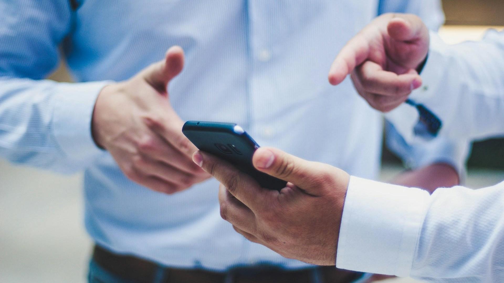 Zwei Männer im Anzug deuten auf ein Smartphone