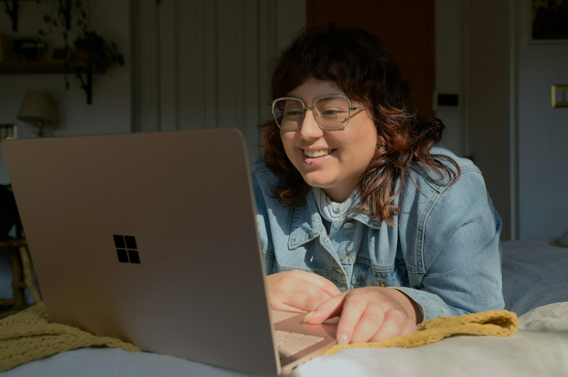Eine junge Frau hat einen aptop vor sich und lächelt.