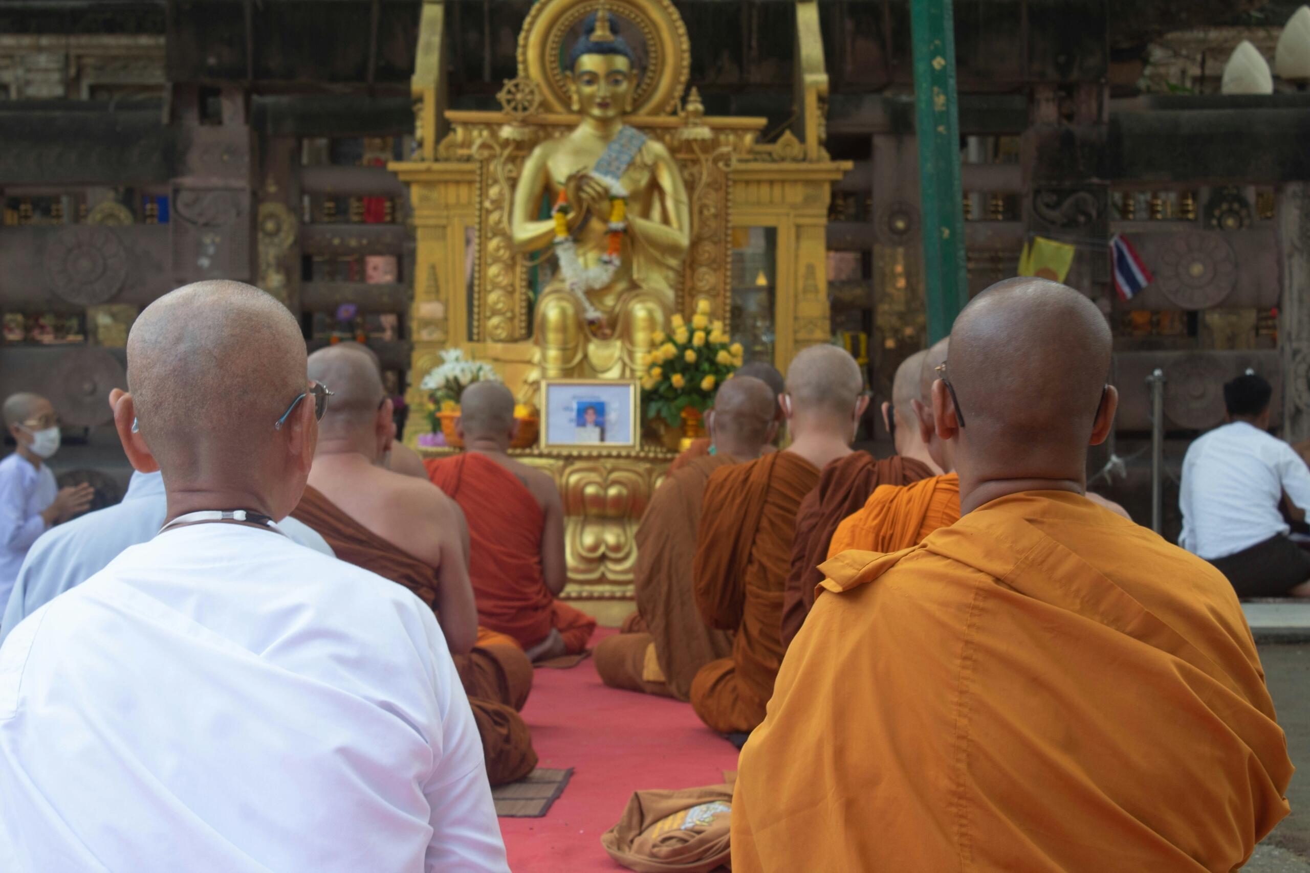 Budistlikud mungad istuvad meditatsiooniasendis kuldse Buddha kuju ees templis