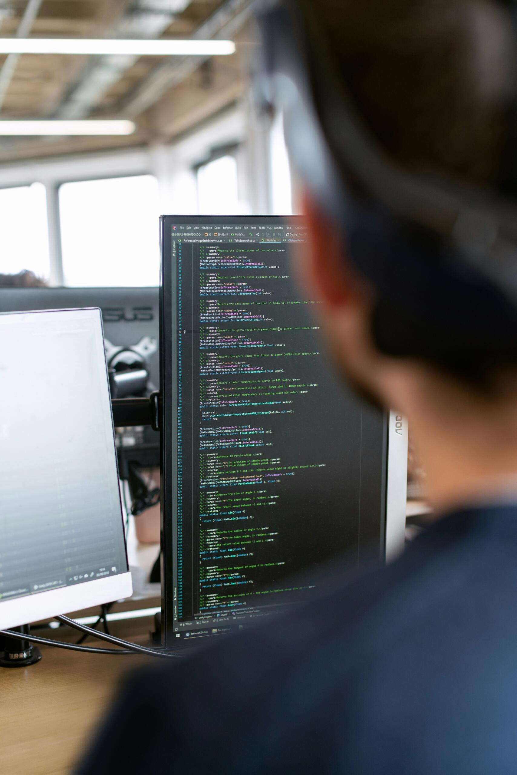 Programmeerija kirjutab koodi kahe monitoriga töölaual