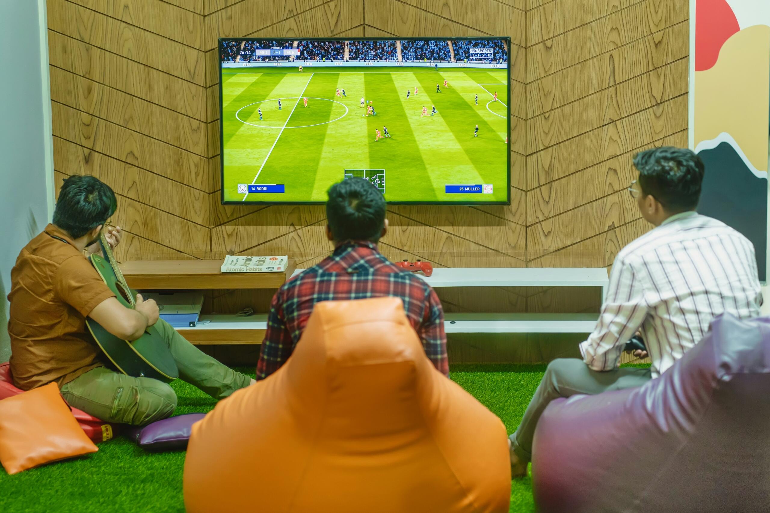 kaks sõpra mängivad koos FIFA jalgpallimängu PlayStationi konsoolil, kolmas mängib klaverit