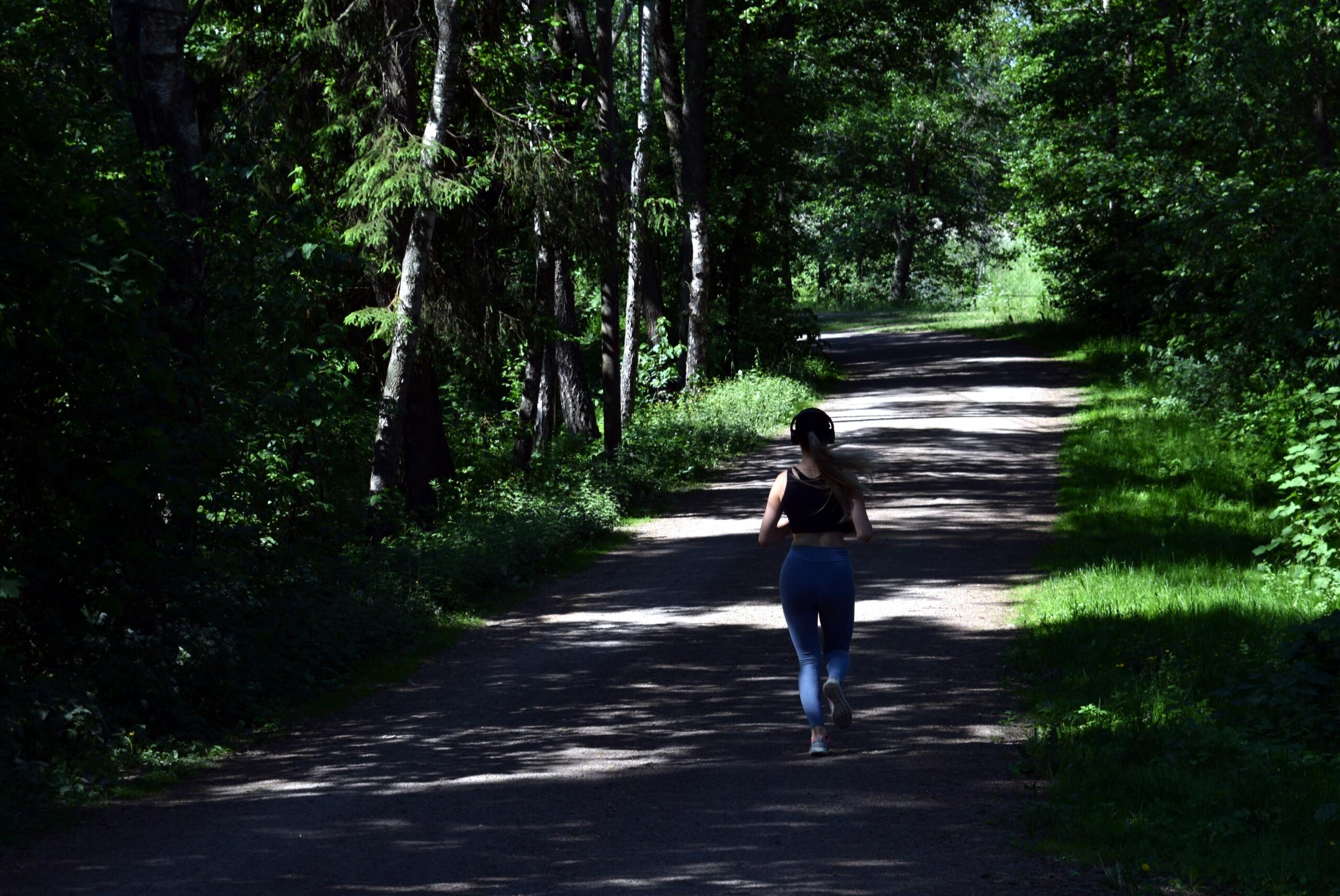 naisjooksja metsavahelisel teel puude vilus