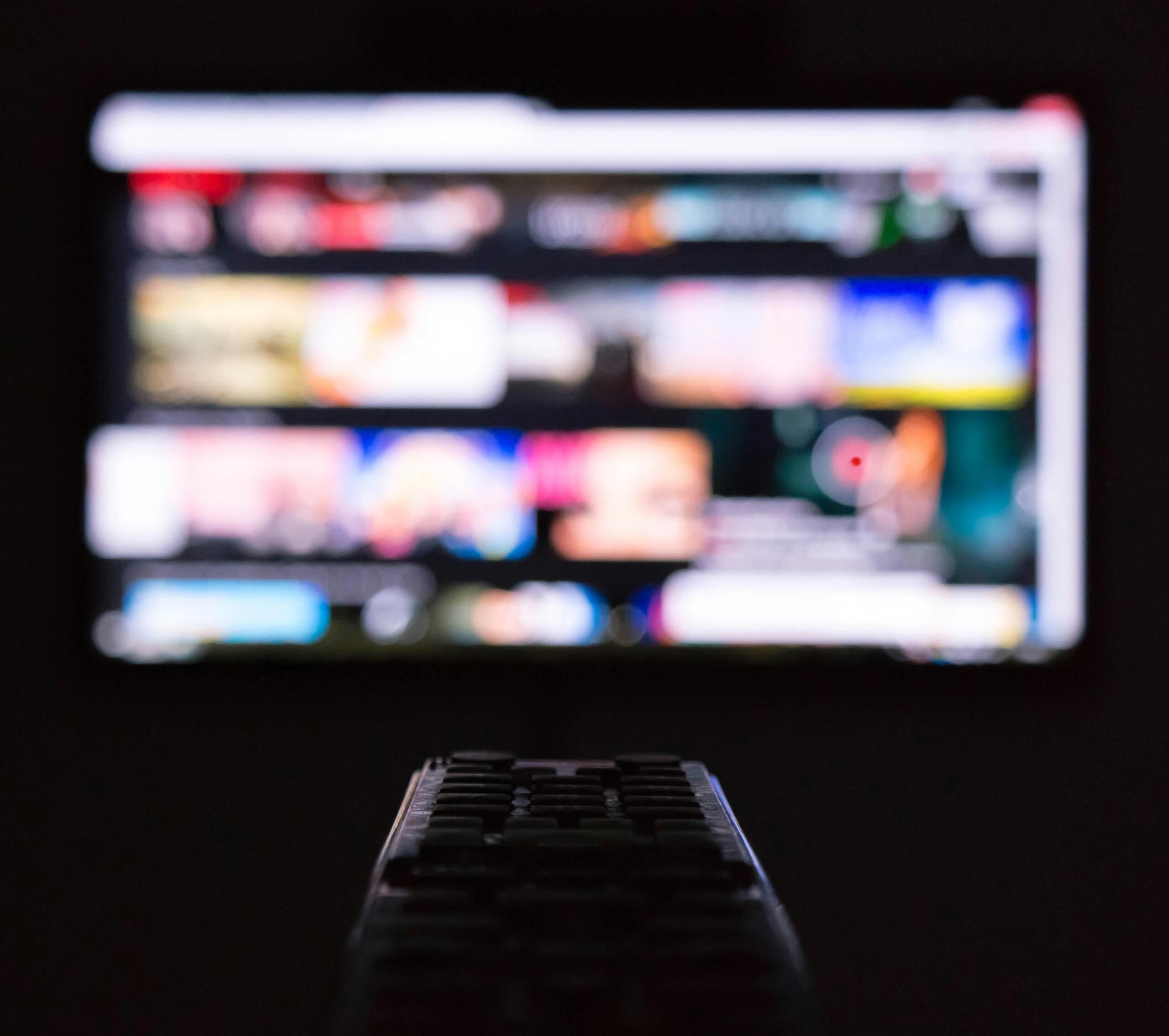 Televiisori pult esiplaanis ja hägune telekaekraan rakenduste ikoonidega taustal