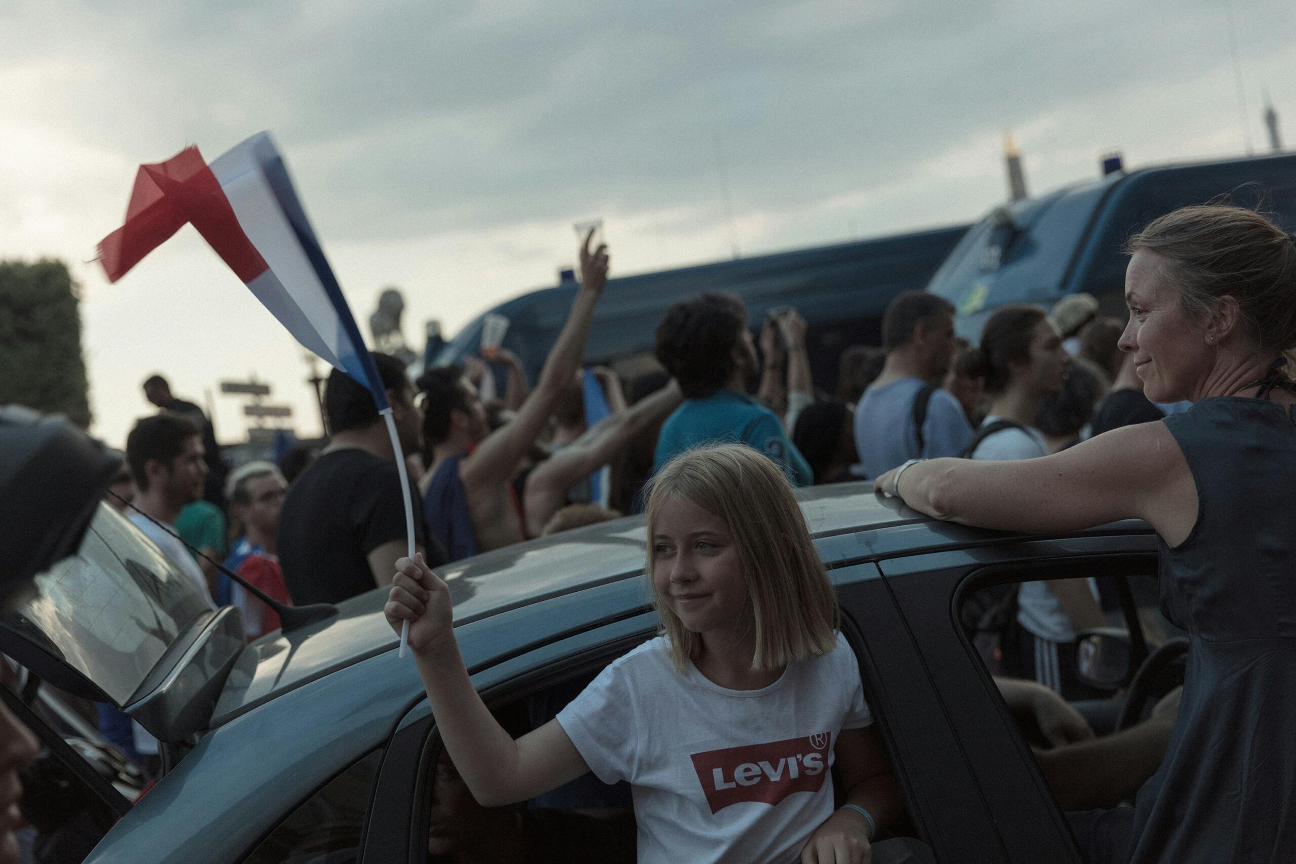 Tüdruk lehvitab autoaknast Prantsuse trikoloori lipuga rahvarohkel tänaval